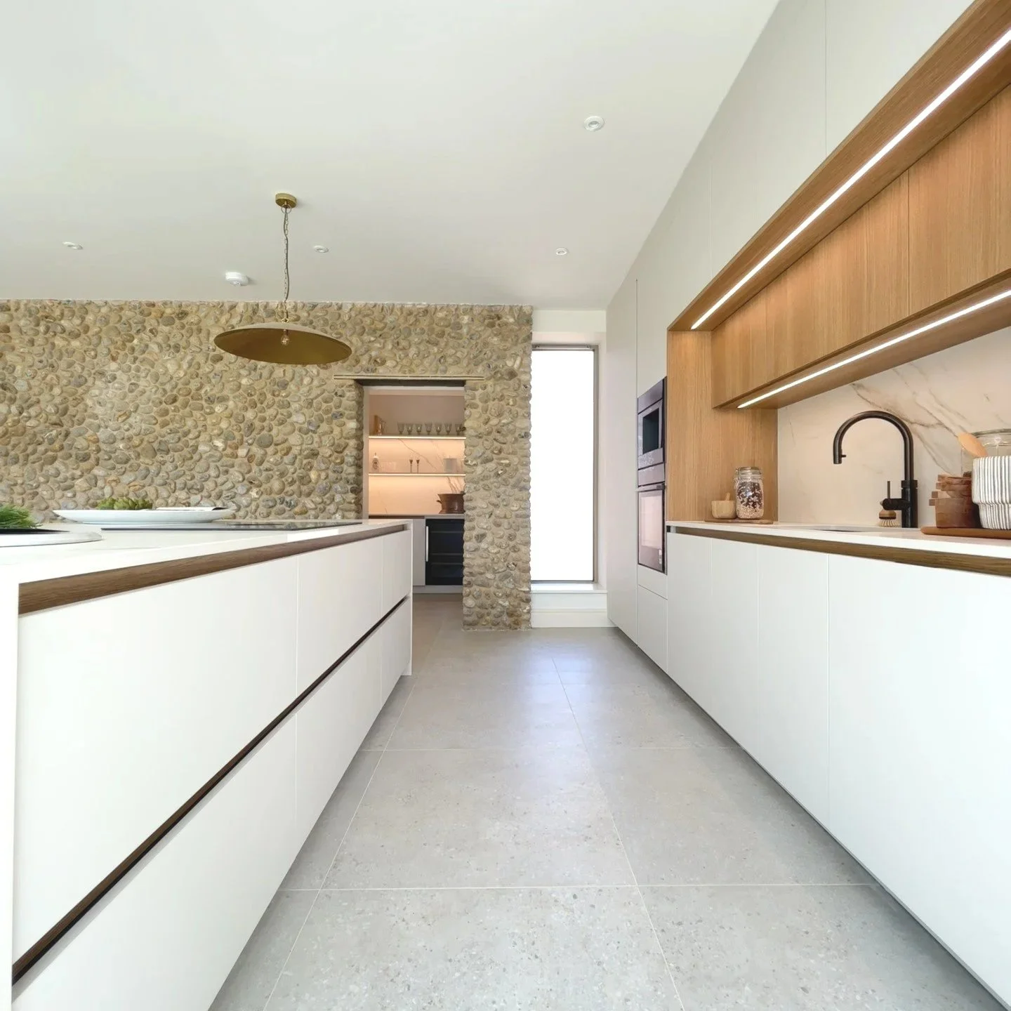 Modern kitchen with white cabinets, wooden accents, a stone wall, and a large window.