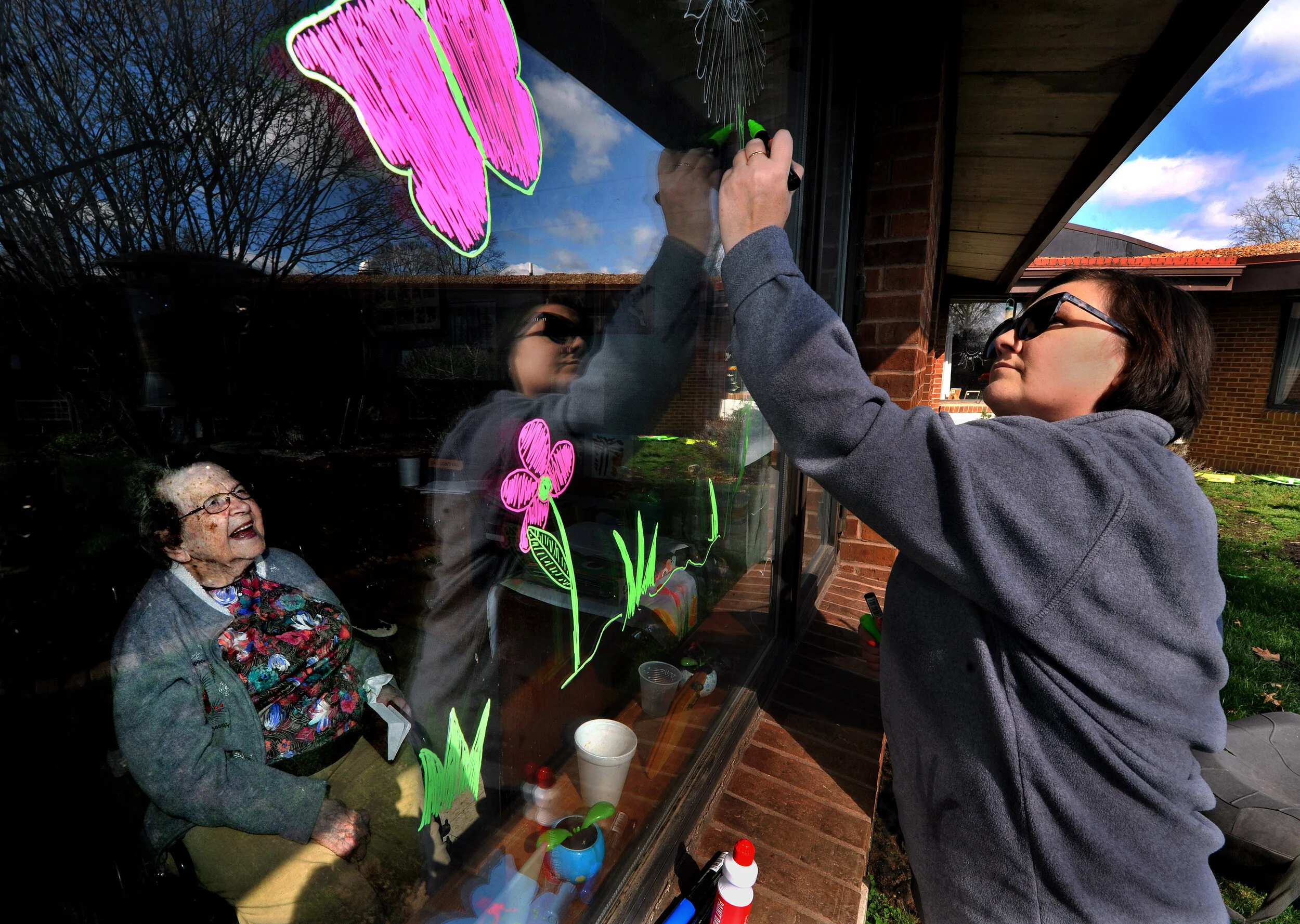 Delores, a 102 year old resident of Eden Village Retirement Home in Glen Carbon, Illinois (left), watches as Dawn Biersborn of Collinsville colors in a butterfly and flowers on her windowon Sunday, March 29, 2020. Because of the Corona Virus, retir