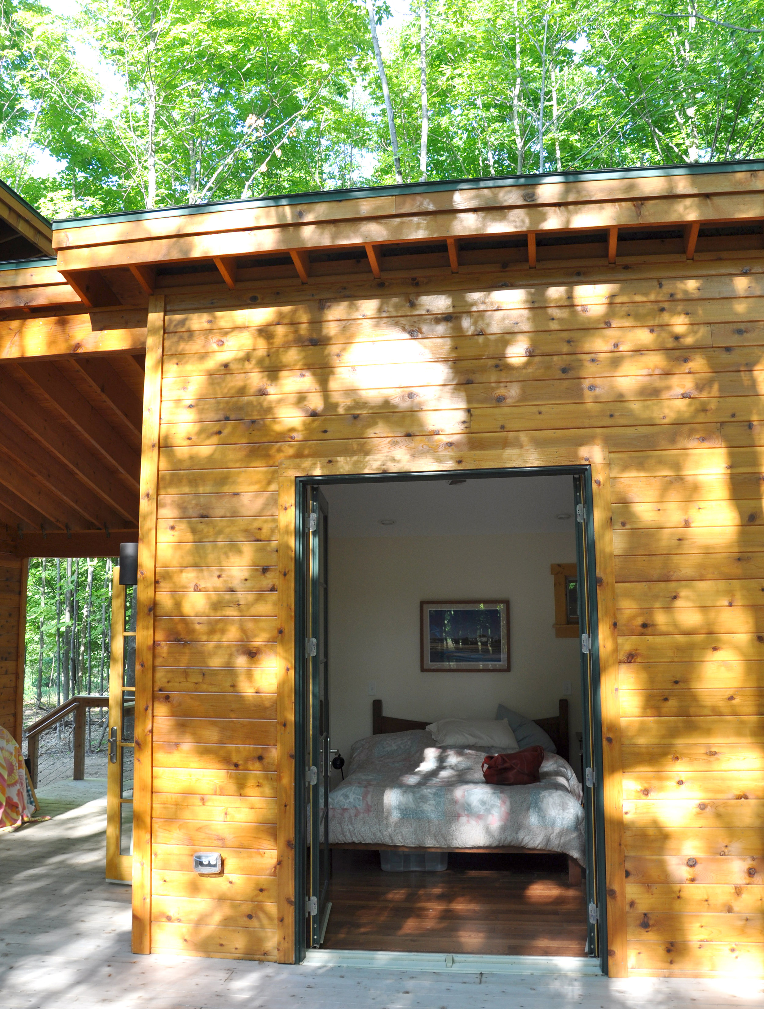 French doors open into primary bedroom suite in a single-family wood-frame vacation house in rural Michigan with a large porch and an energy-efficient, sustainable green design