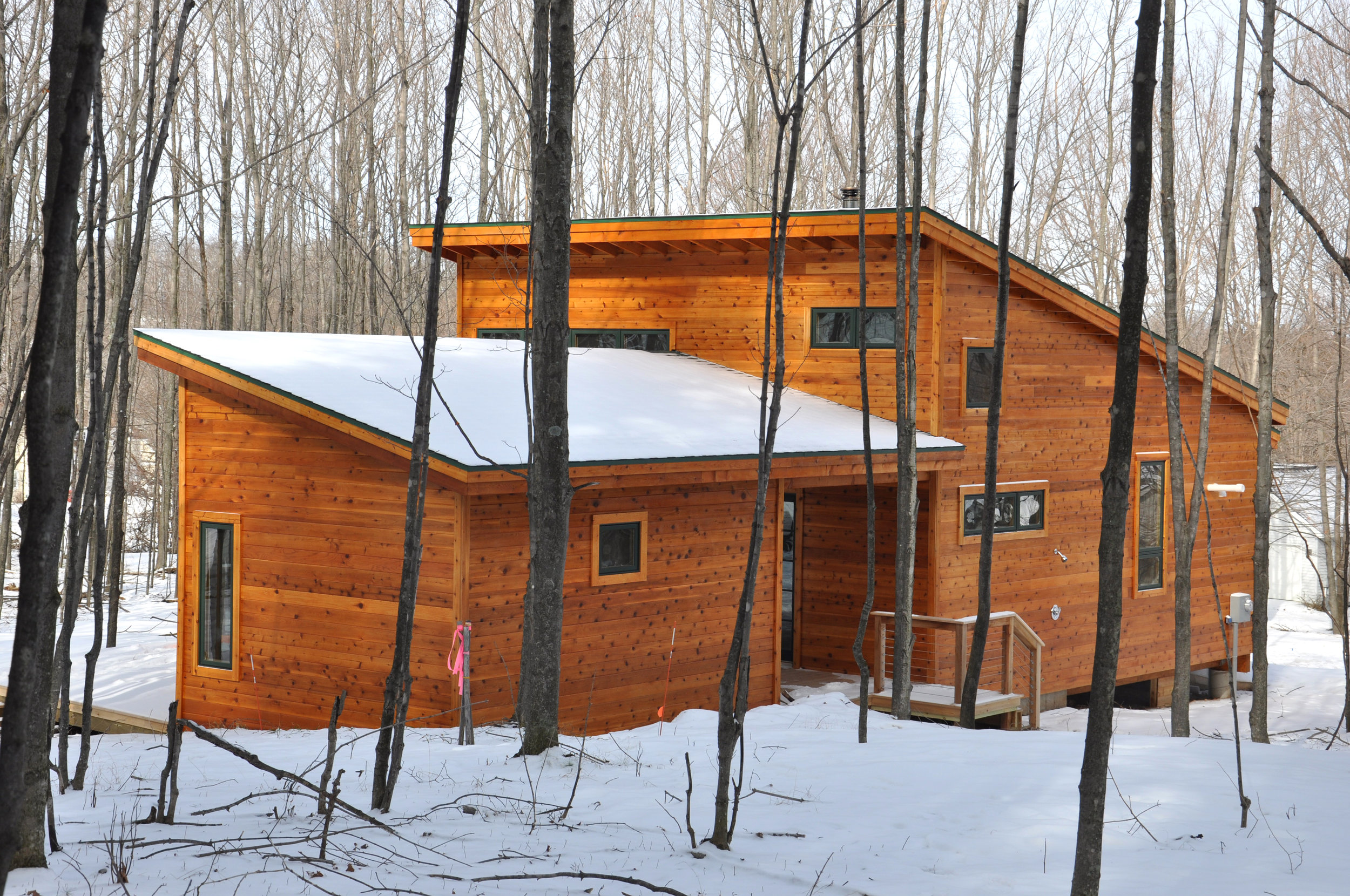 exterior winter view of a newly constructed single-family wood-frame vacation house in rural Michigan with a large porch and an energy-efficient, sustainable green design