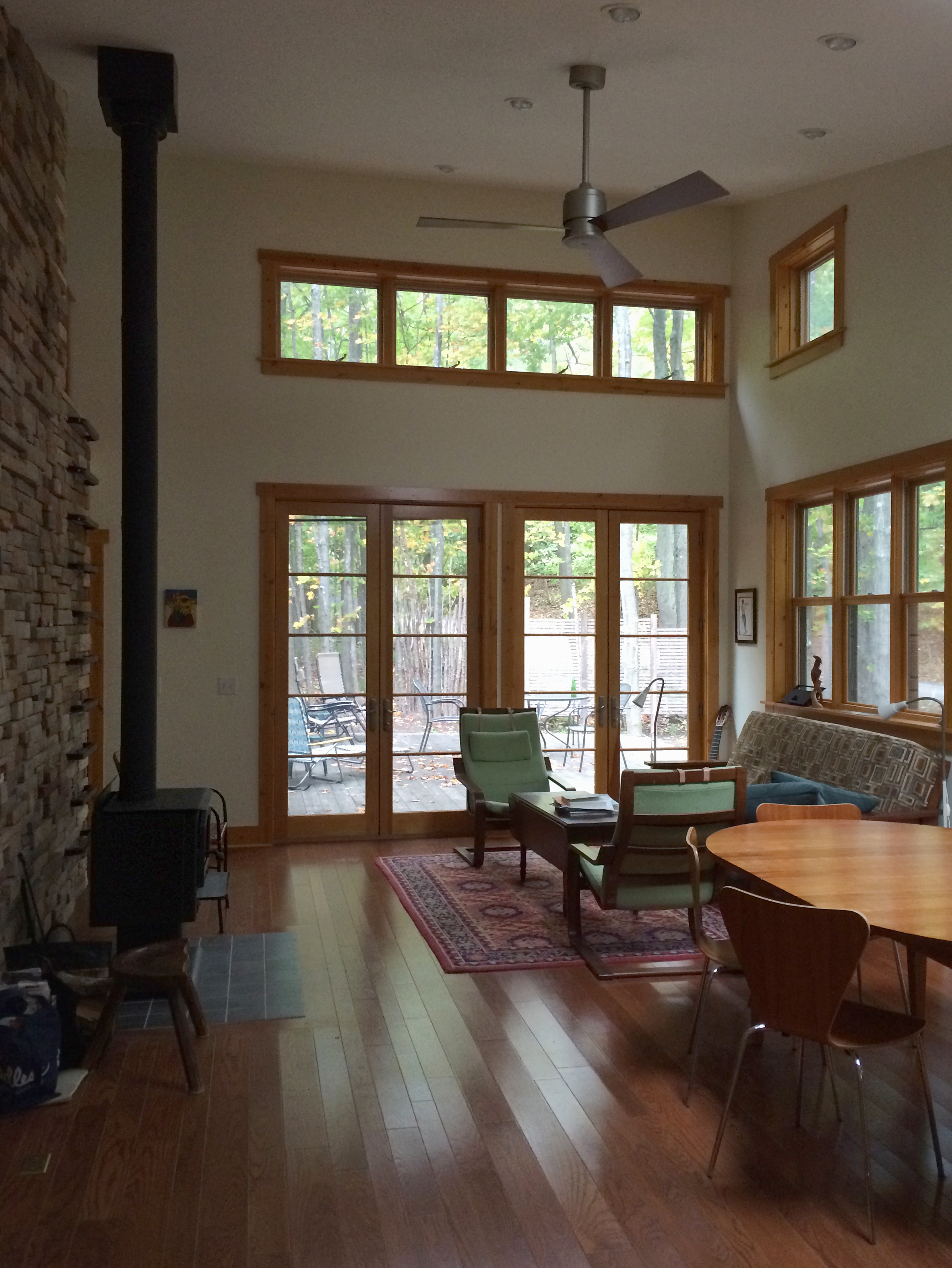 Open-plan living area with a wood stove and french doors that open to a large patio in a rural, wood-frame, energy-efficient vacation home 