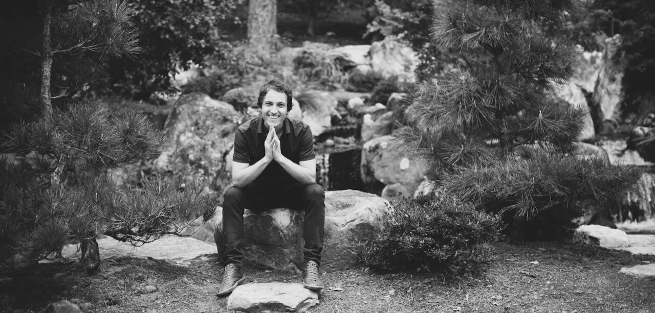Simon Spire sitting in a rock garden and smiling.
