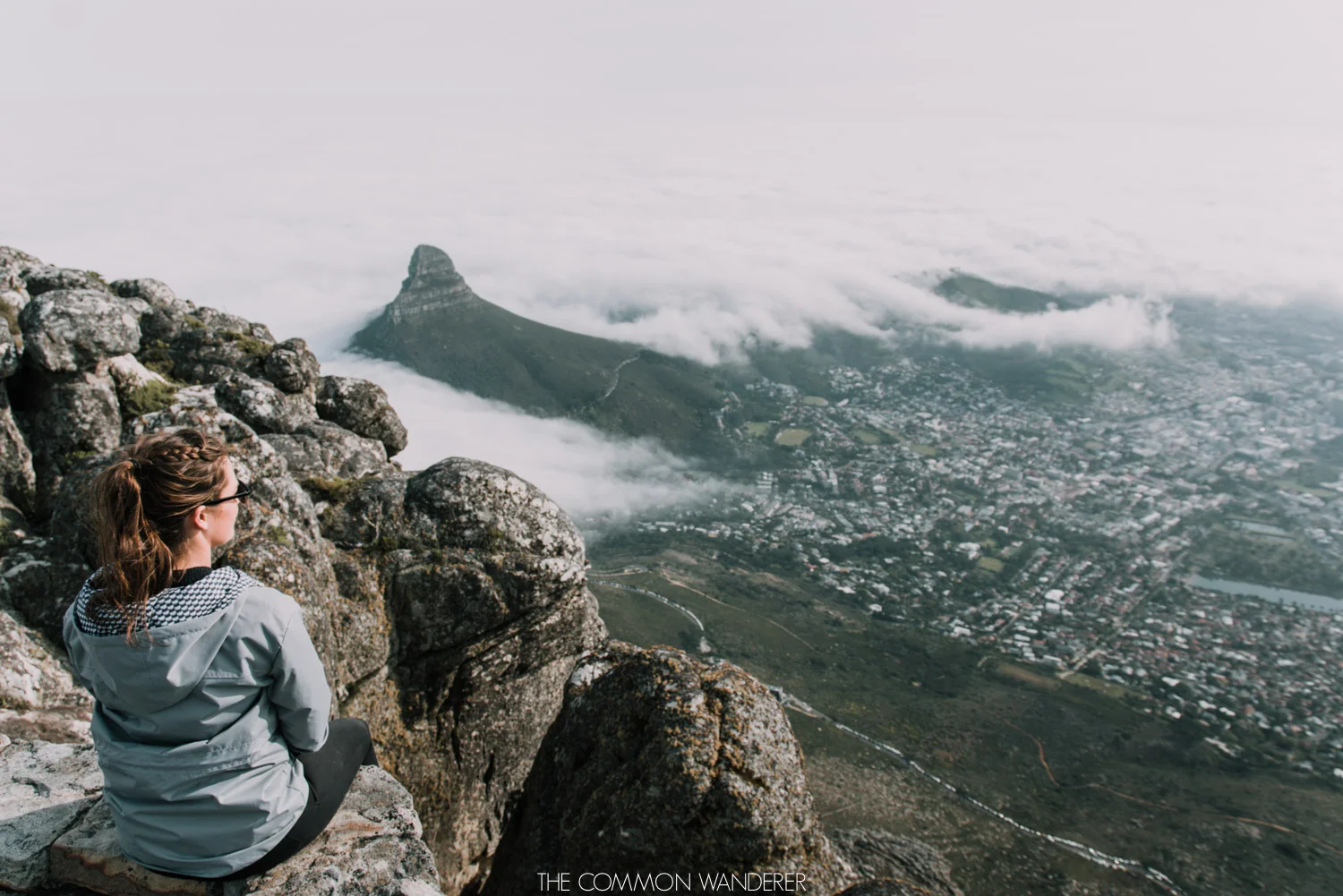 A woman sits on the edge of Table Mountain, Cape Town - The Common Wanderer