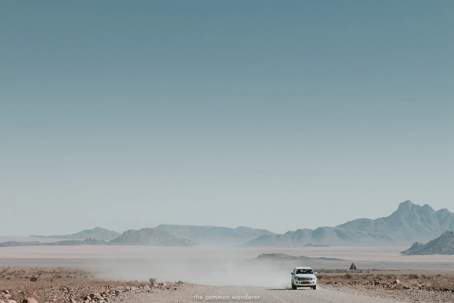 A car driving along a long dirt road in Namibia