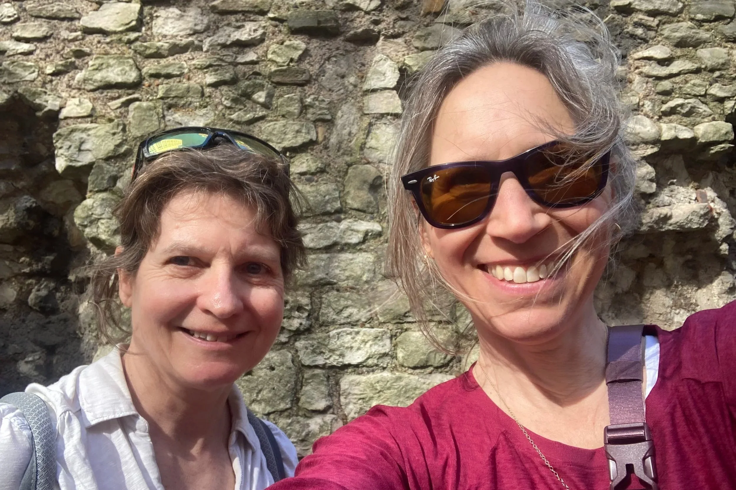 Penny and Caroline smiling in front of a stone wall, capturing a moment on the Race Across The World Experience in London.