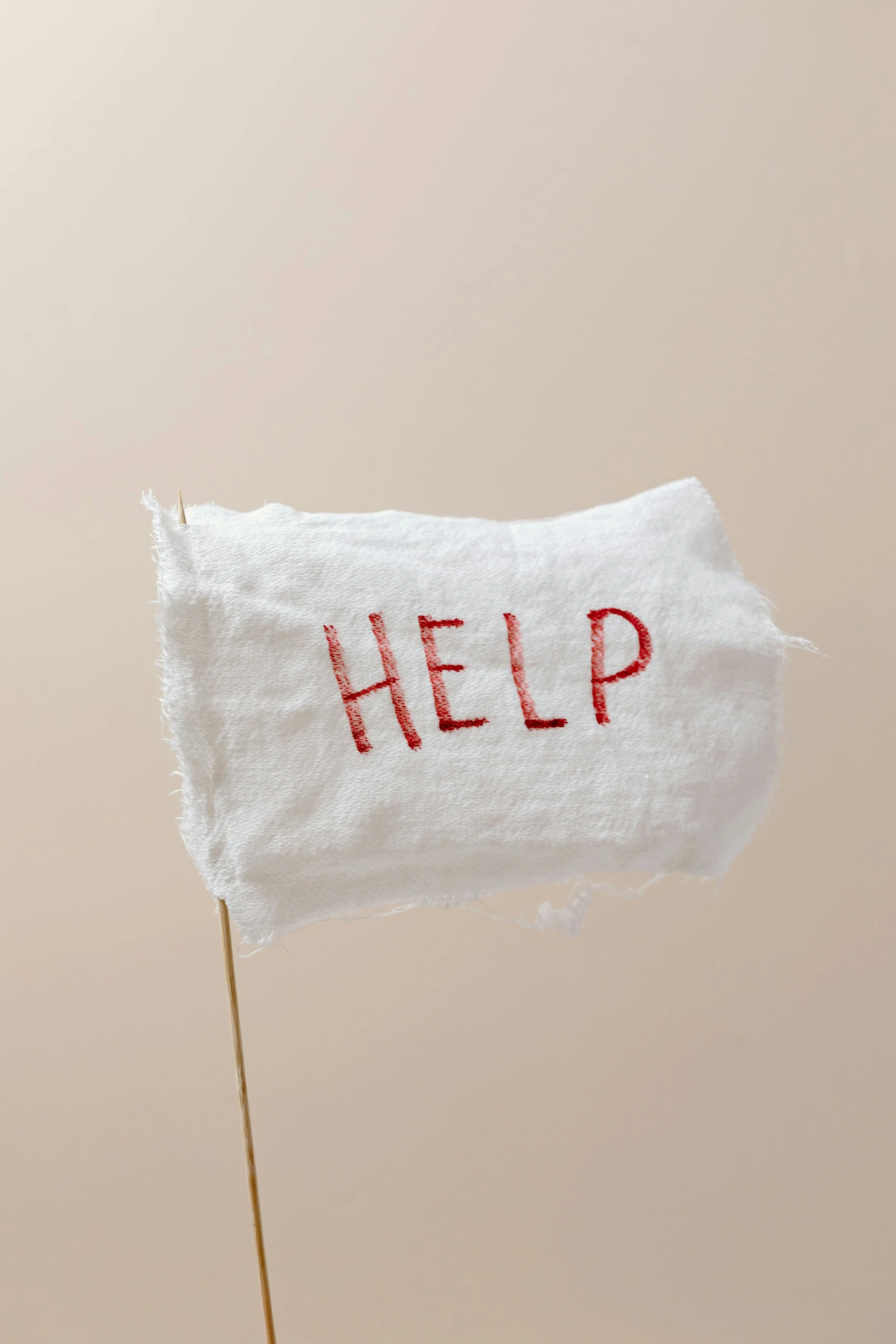 White piece of cloth attached to a cocktail stick with the word "HELP" in red font against a beige background