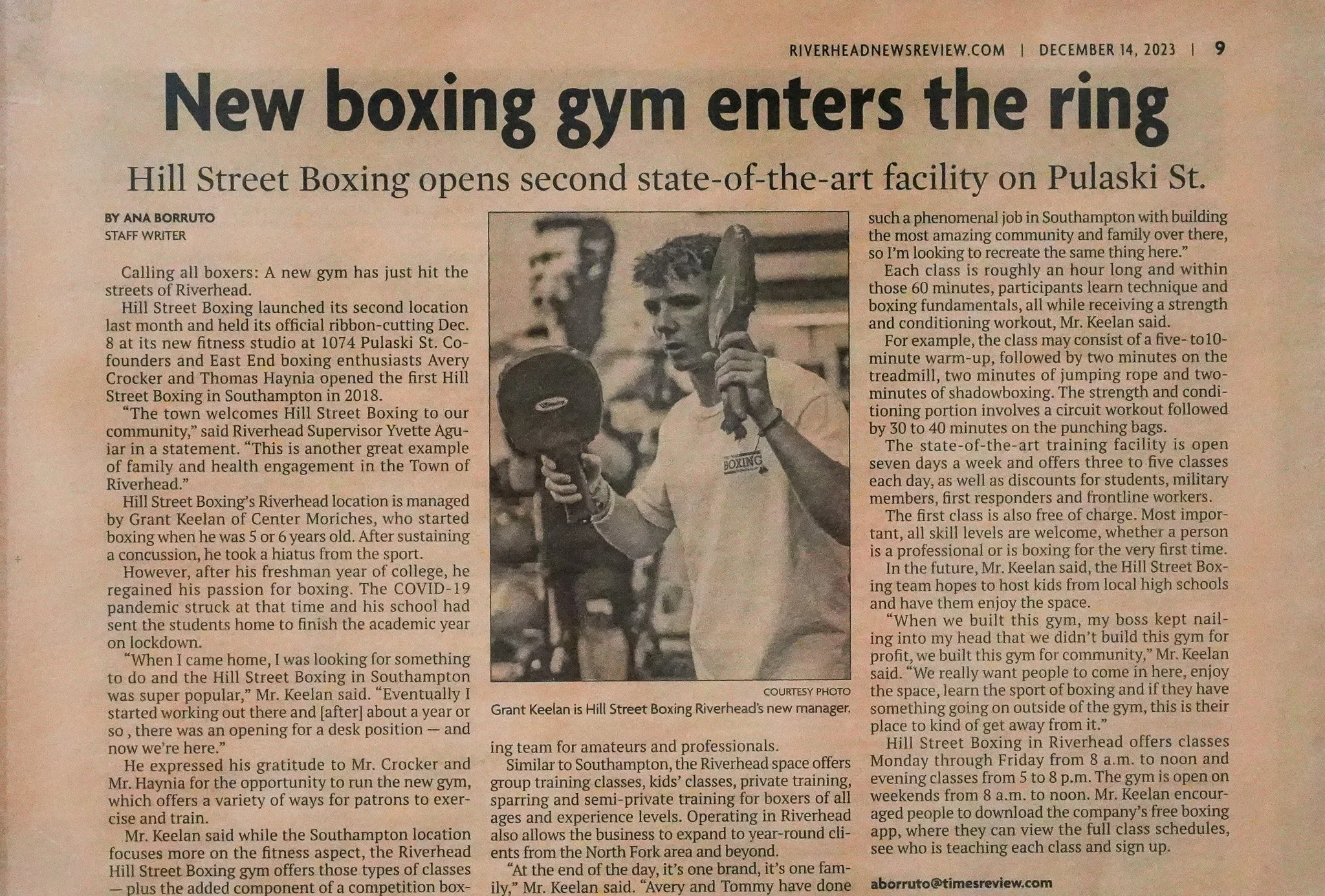 Black and white photo of a man wearing a white t-shirt with 'Boxing' written on it, holding a boxing glove in one hand and a towel over his shoulder.