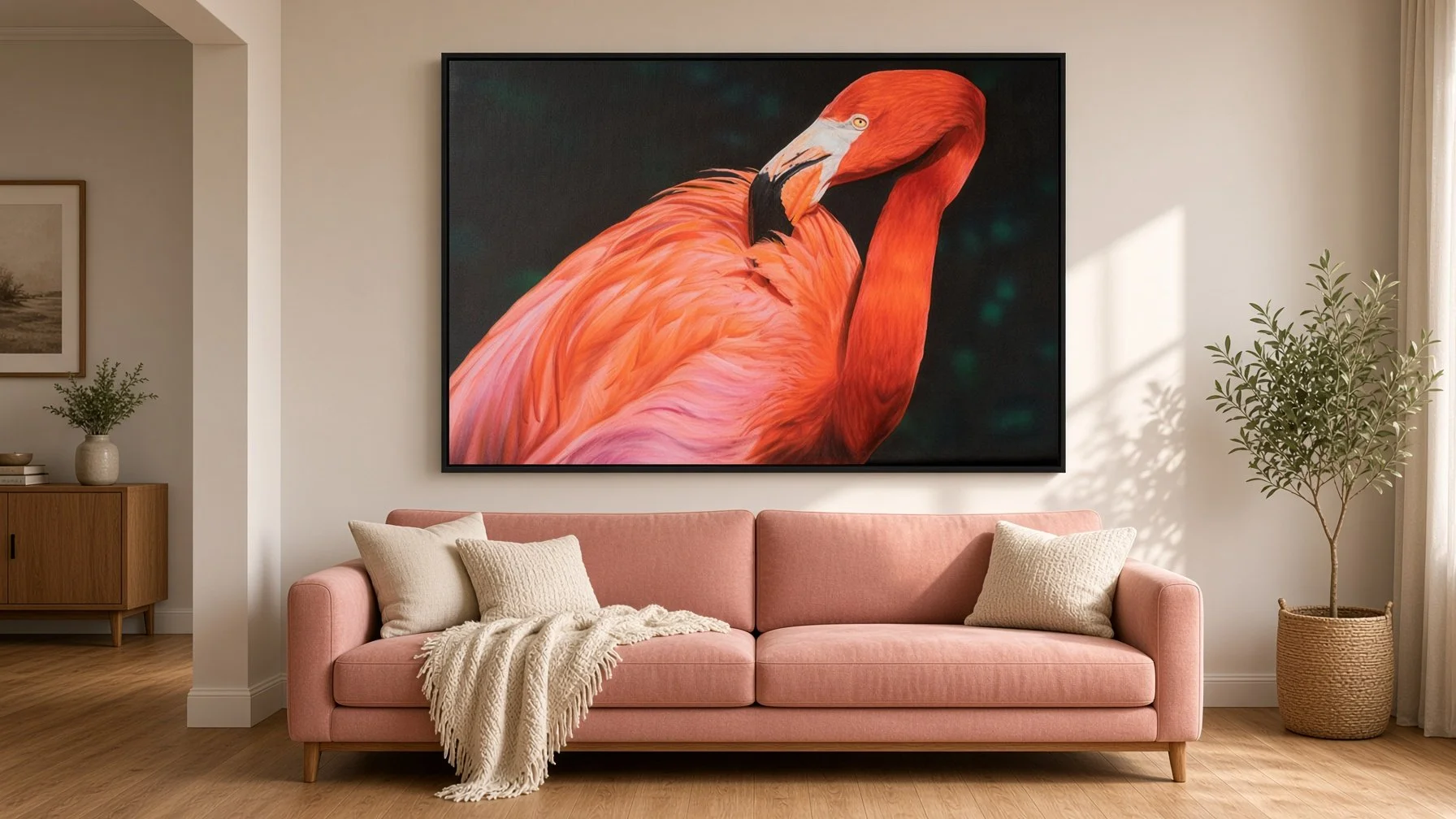 Living room with a pink sofa, beige pillows, a cream blanket, a large flamingo artwork on the wall, a potted plant on the right, a small potted plant and framed picture on the left side of the wall.