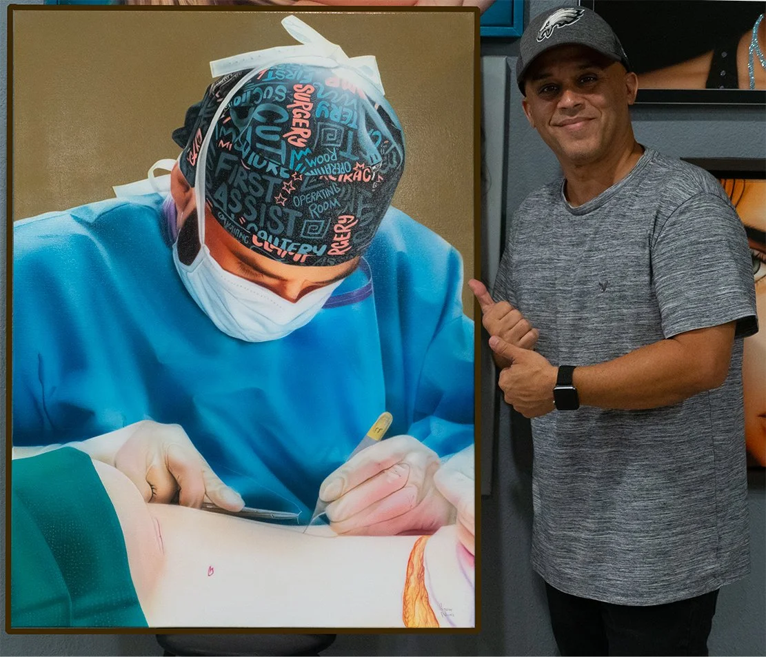A man wearing a gray t-shirt, a gray cap with a sports logo, and a watch, pointing to a large portrait of a surgeon performing a medical procedure.