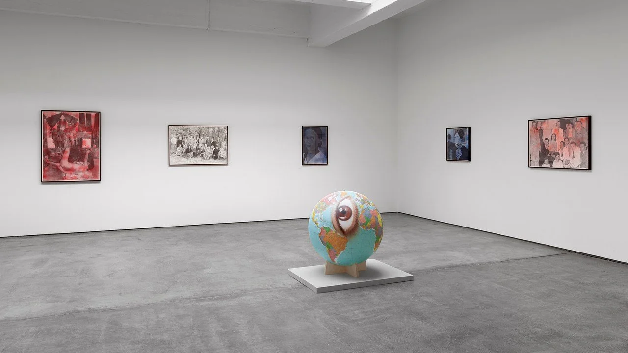 Contemporary art gallery with framed pictures on white walls and a globe sculpture with an eye in the center on a pedestal