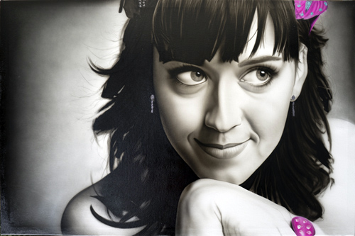 Black and white portrait of a woman with dark wavy hair, bangs, and a playful expression, wearing earrings and with pink accessories edited onto the image.