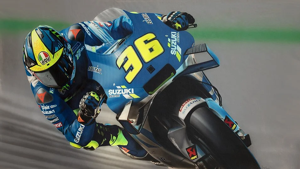 Motorcycle racer in blue racing suit leaning into a turn, riding a Suzuki motorcycle with the number 36 on it.