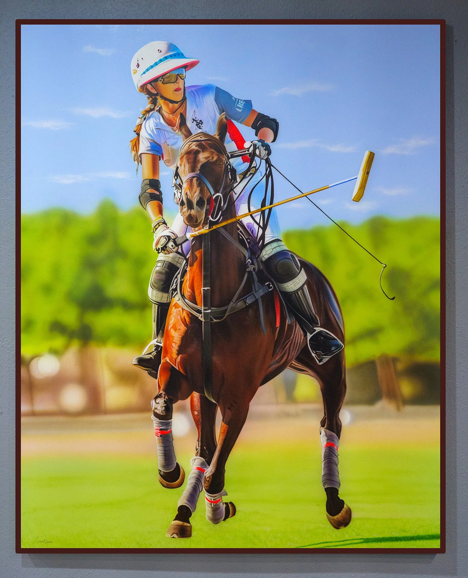 A woman participating in horse jumping, wearing a helmet, goggles, and athletic attire, riding a jumping horse over an obstacle on a grassy field with a blue sky in the background.