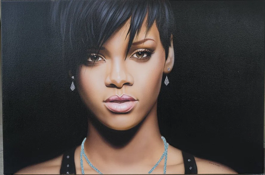 Close-up portrait of a woman with short black hair, wearing diamond earrings and a blue necklace, against a dark background.
