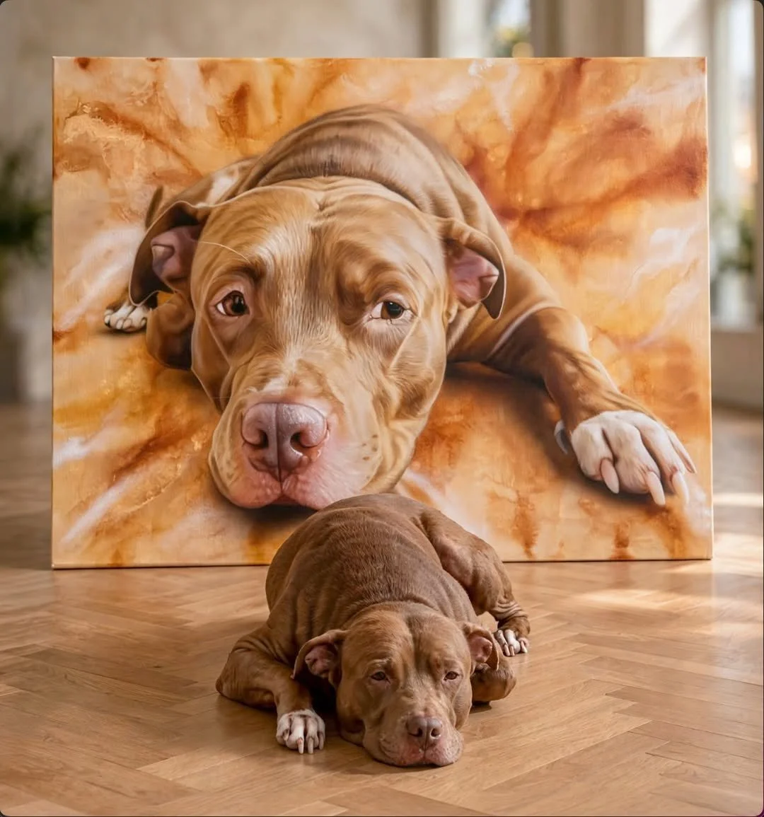 A brown puppy lying on a wooden floor in front of a large painting of a dog with similar coloring, lying on a beige and orange background.