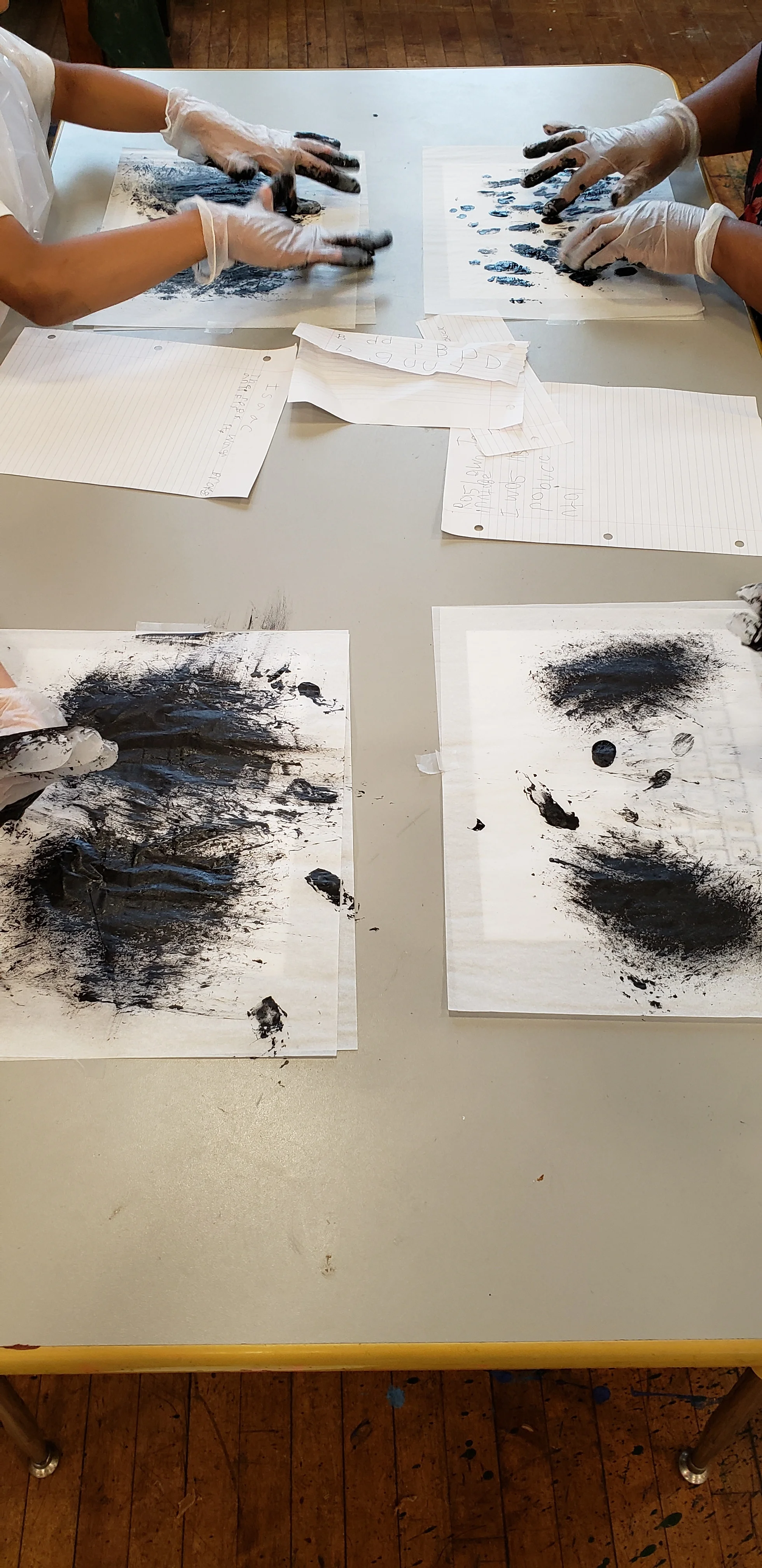 On the art room tables students hands can be seen covered in gloves and black paint “typing” on the tracing paper.