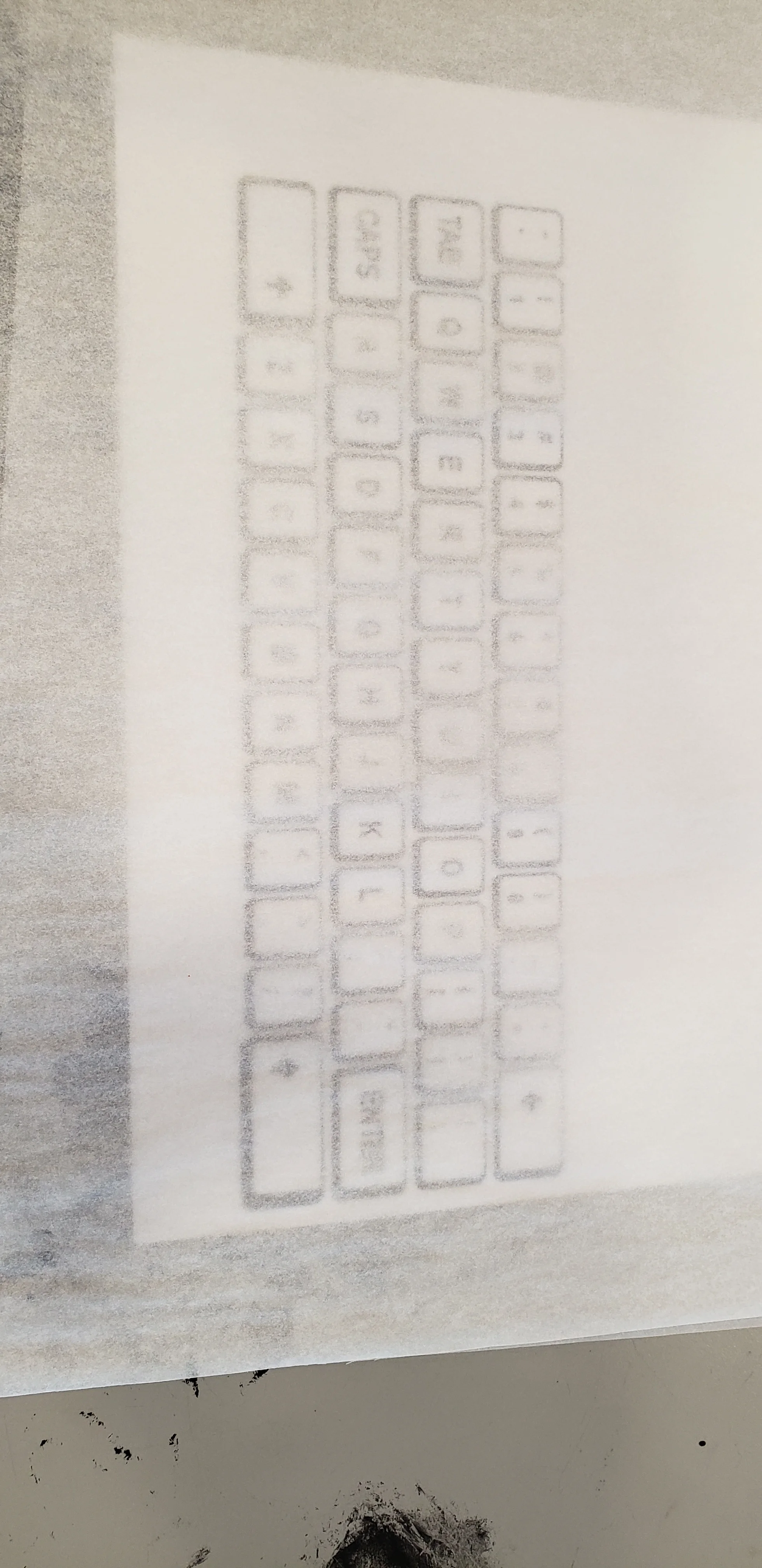 Close up of the art room table, the keyboard print outs are now covered by a piece of tracing paper so that the keys themselves are still visible.