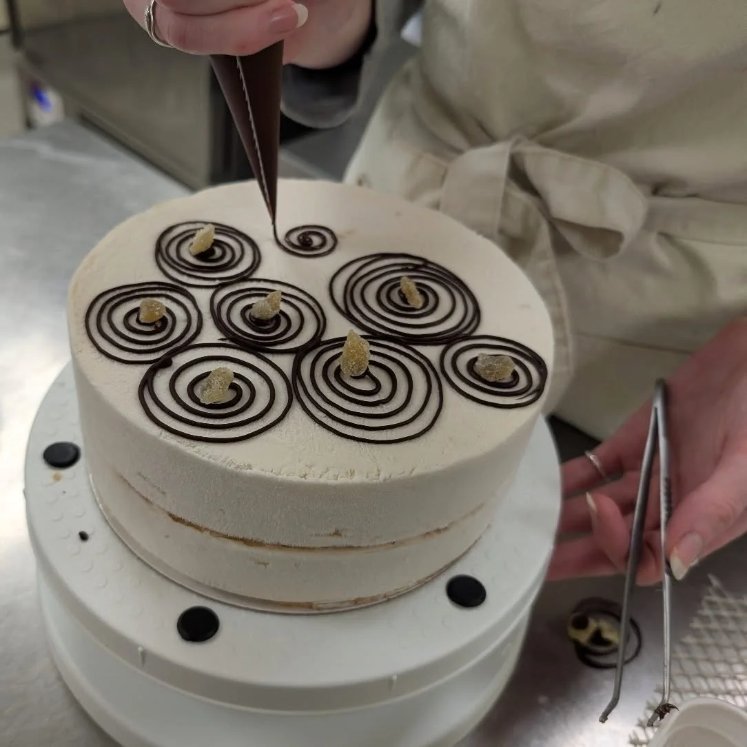 Your cakes are all coming along nicely. Lowri has been working so hard to get them all together, and here she is just casually free-handing chocolate swirls. She has been decorating everything so beautifully and all in the same week as fielding our f