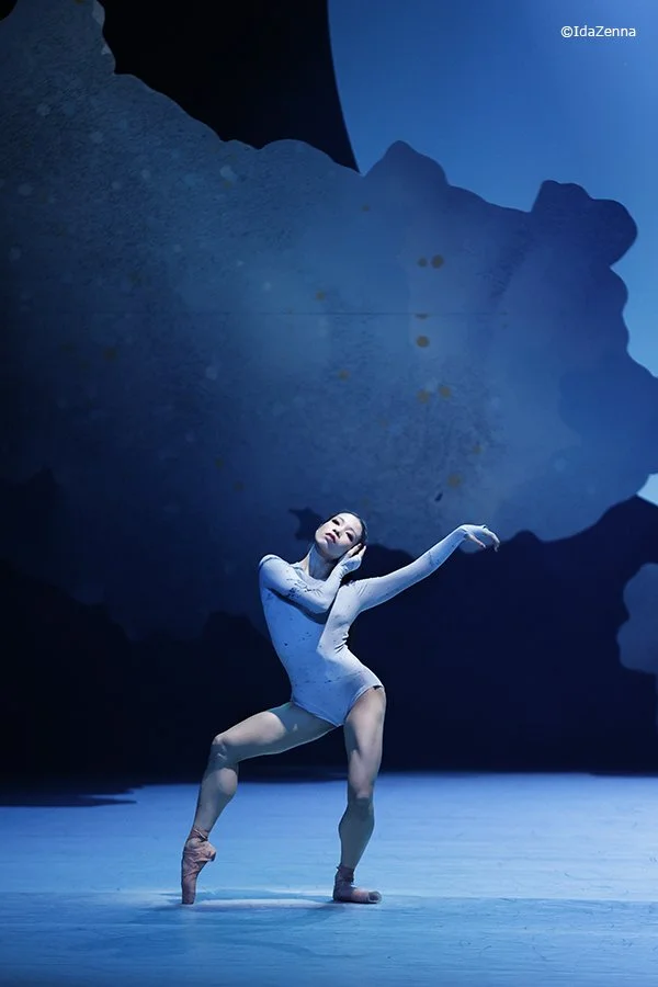 Ballet dancer performing on stage with a blue abstract background.