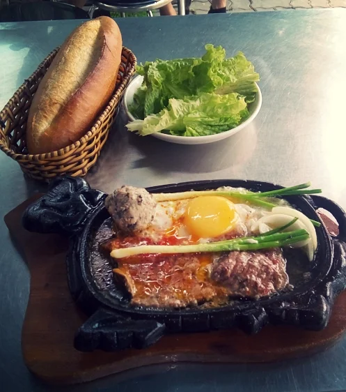 Medium-rare steak, runny-yolk egg, pork and mushroom meatball and sauteed onions on a sizzling plate, warm baguette, lettuce for some reason, and my attempt at using a photo filter.