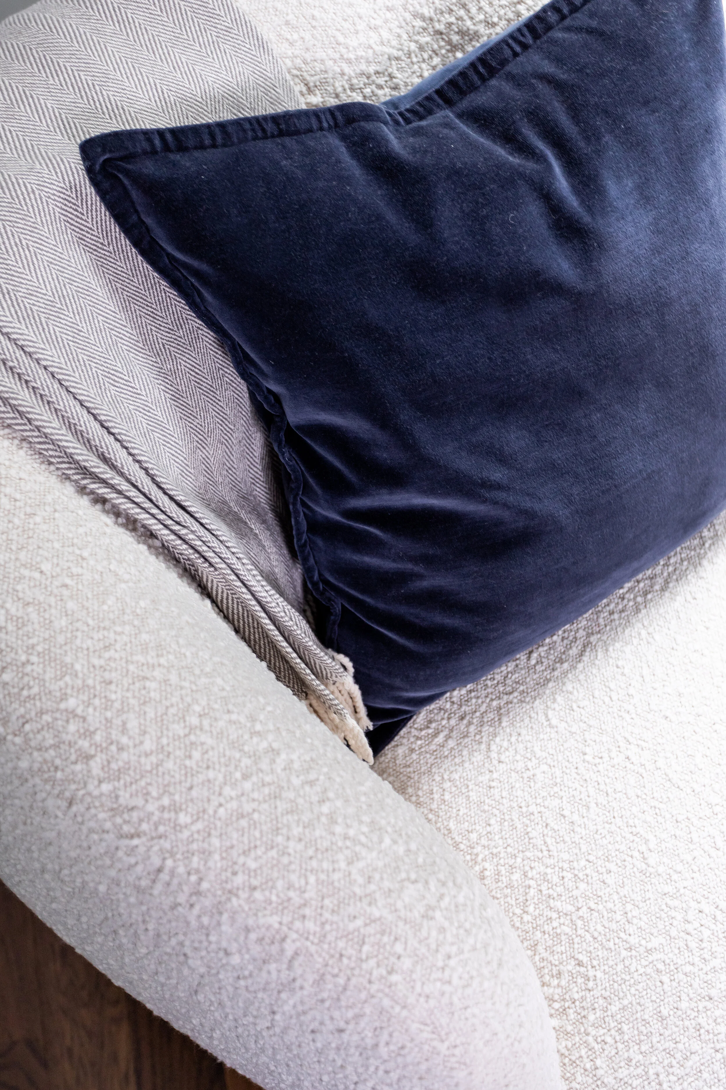 Deep blue velvet throw pillow and gray herringbone wool blanket layer on top of an off-white boucle upholstered swivel lounge chair in the Main Bedroom.