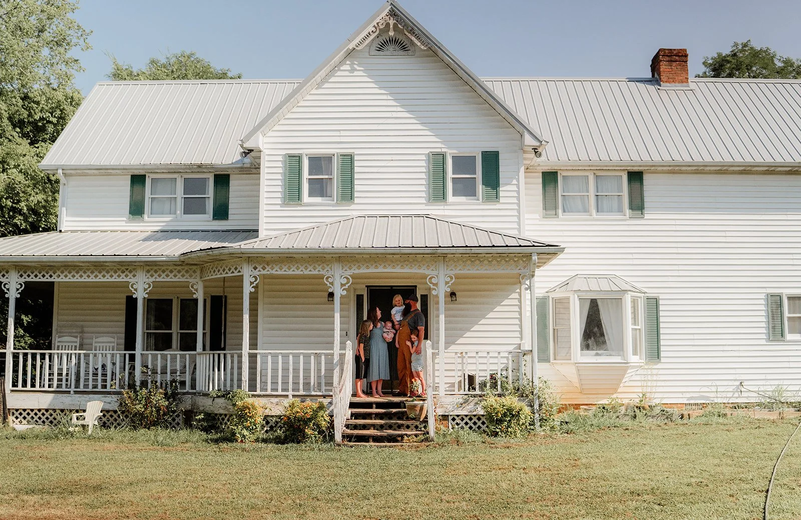 Family standing on the porch of a white farmhouse smiling at each other