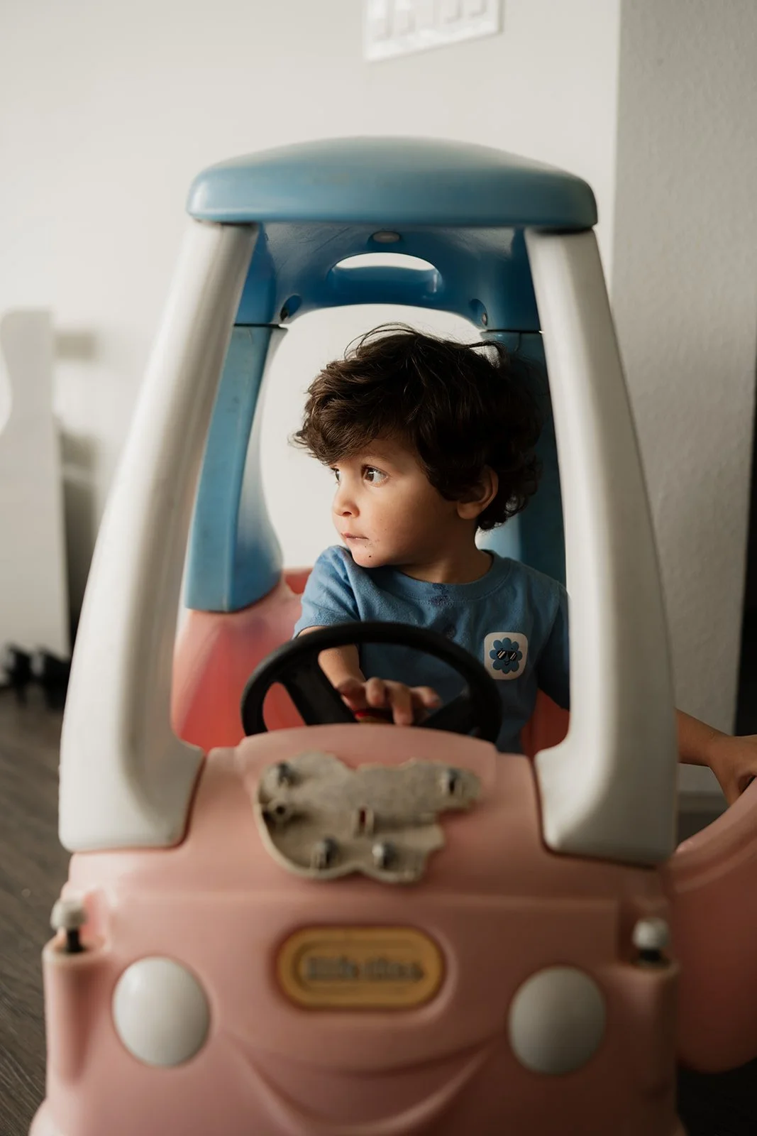 Little boy sitting inside of a little tikes car looking away