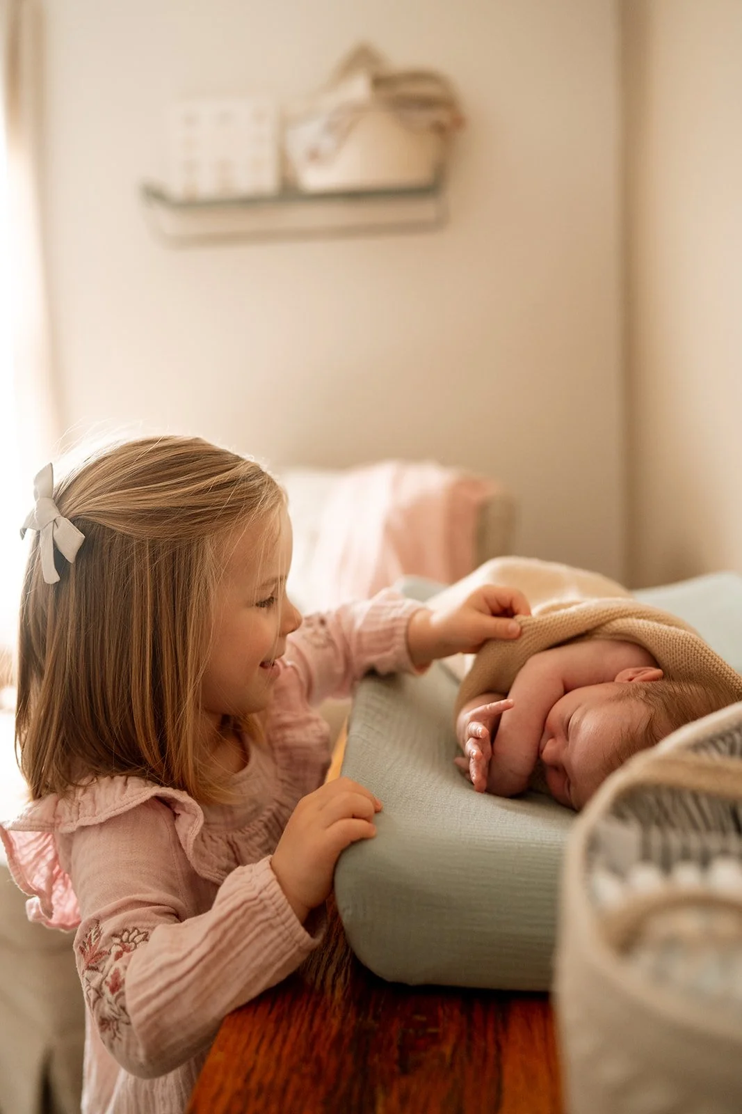 little girl with bow in her hair smiling at her baby sister on the changing table