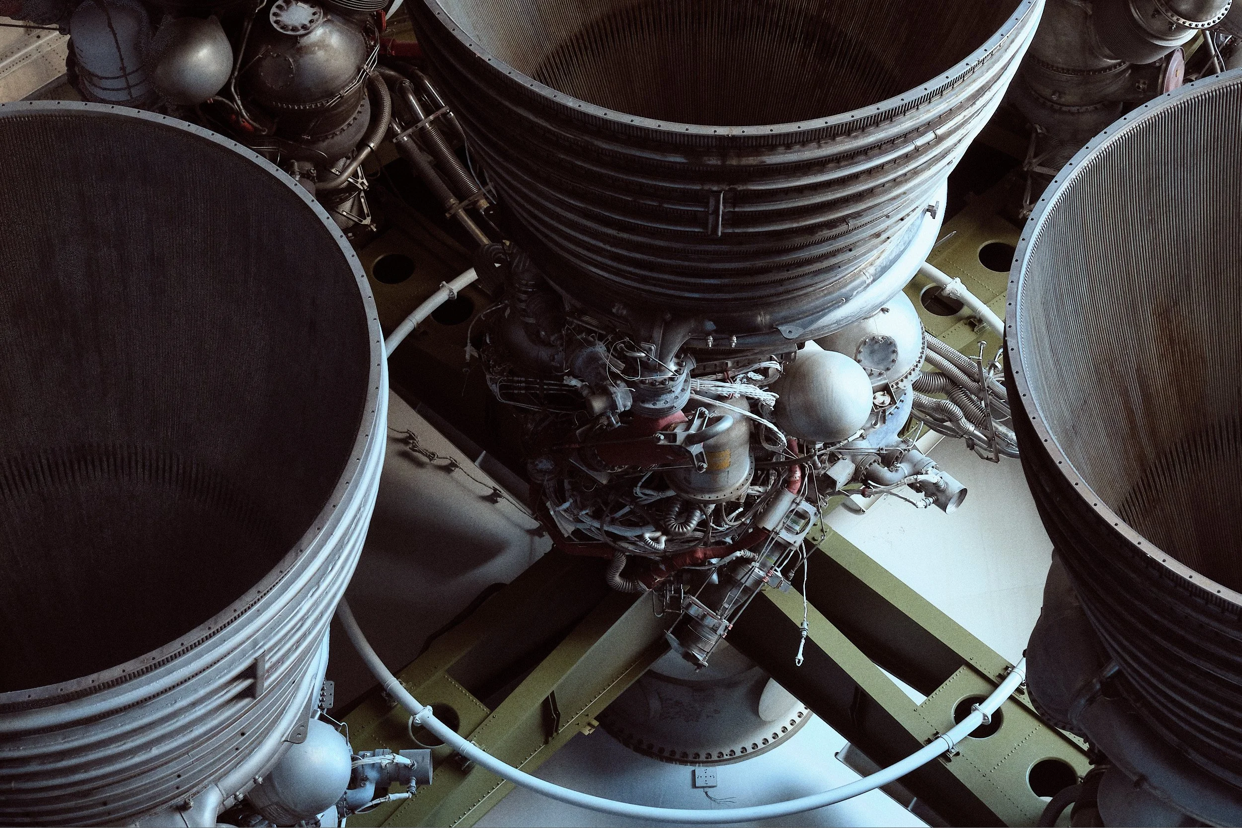 Close-up view of a rocket engine with three large exhaust nozzles, showcasing intricate mechanical components, pipes, and metal surfaces.