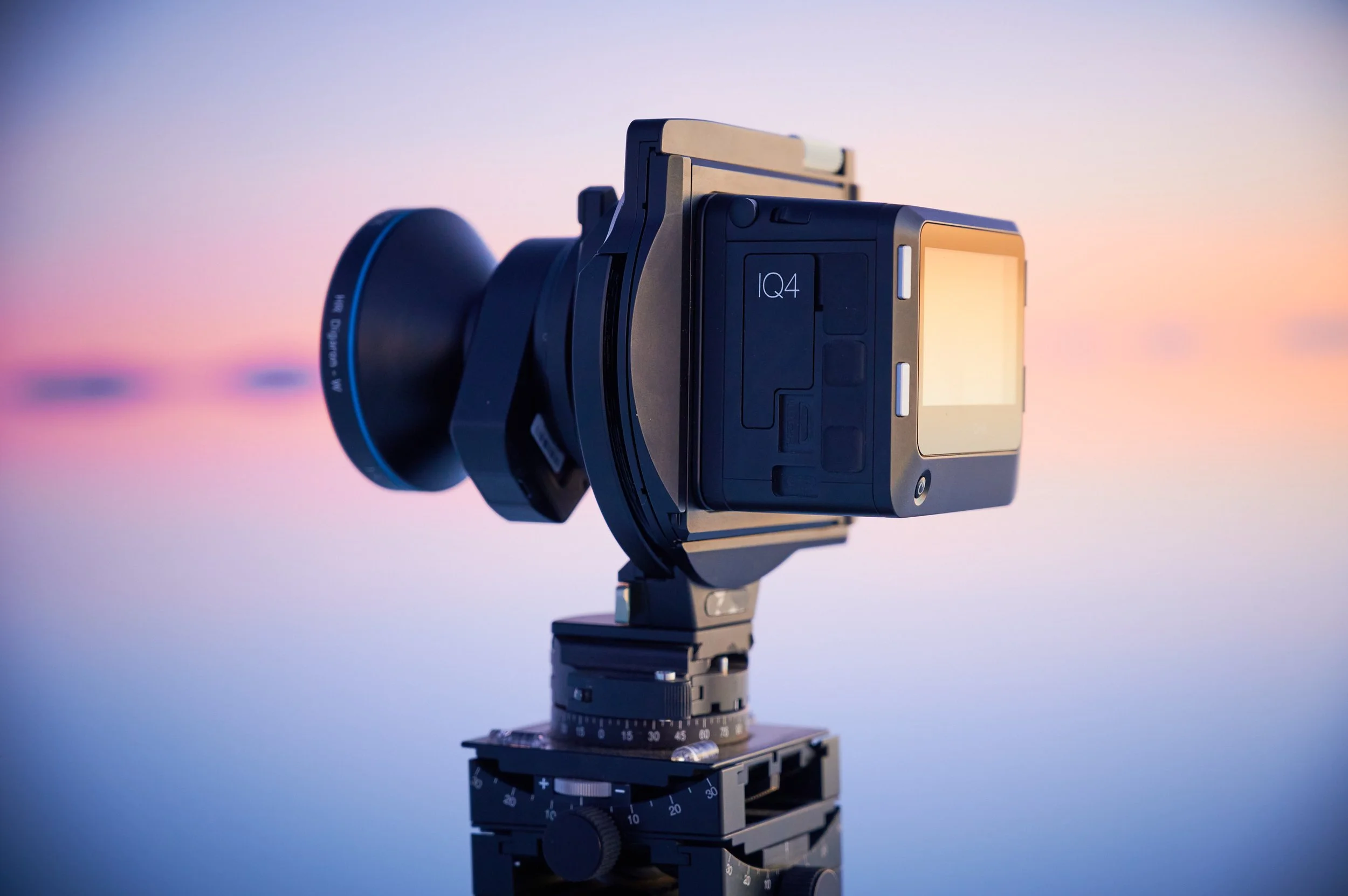 A professional camera mounted on a tripod against a colorful sunset sky.