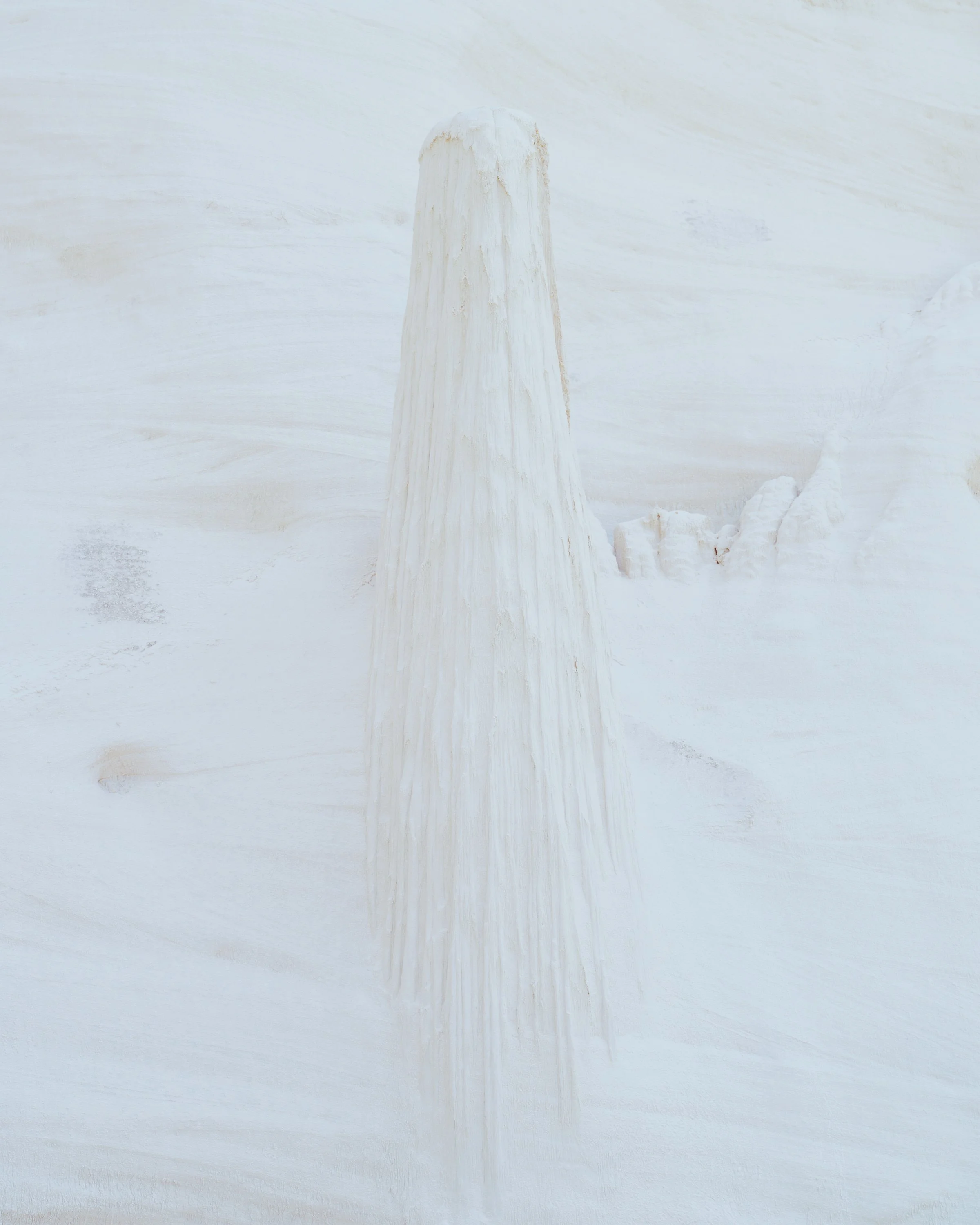 A large, white, elongated stalactite or mineral formation hanging from a ceiling in a cave or cavern.
