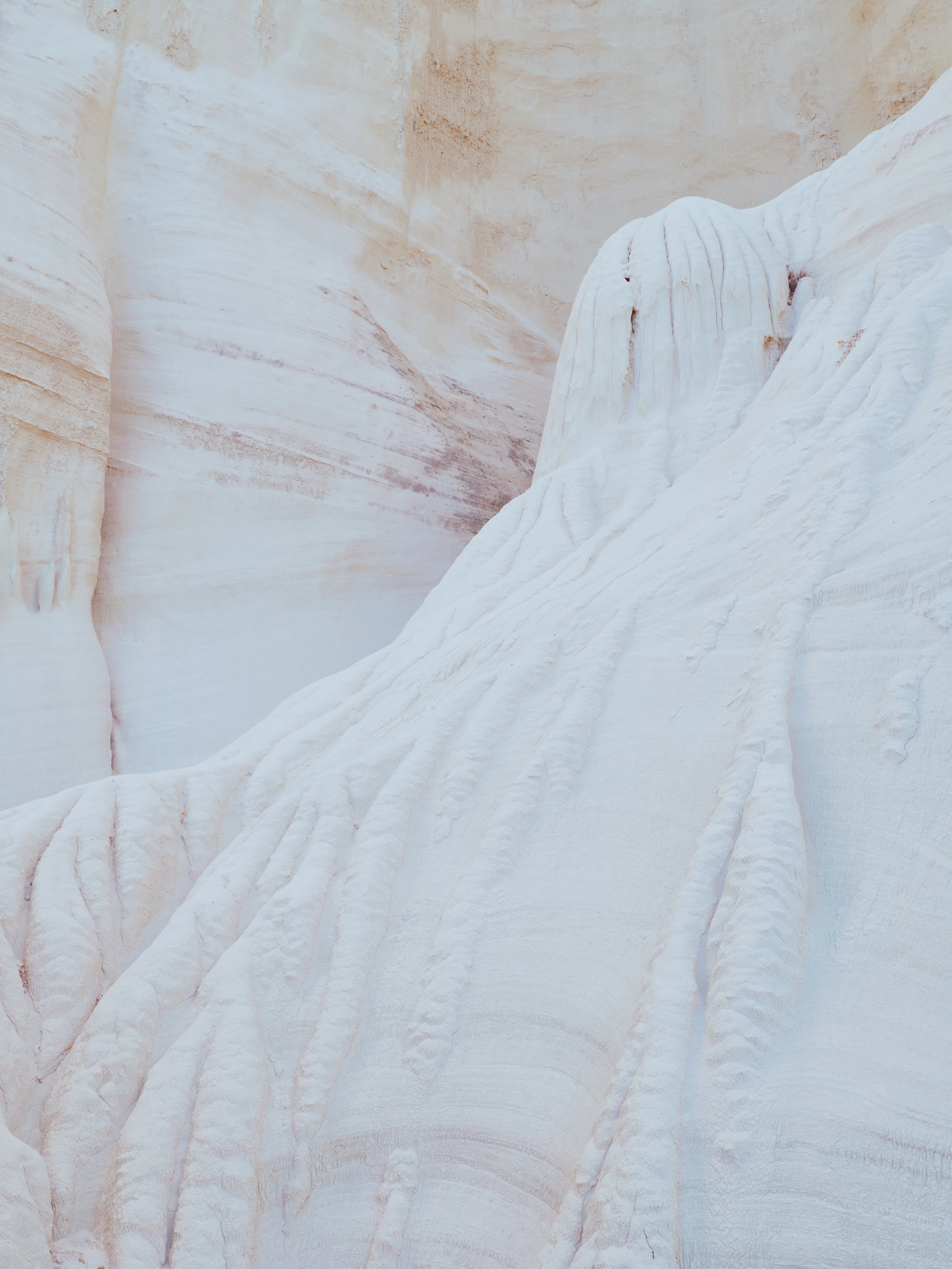 Close-up of white and peach-colored layered sandstone formations with smooth, flowing textures and visible striations.