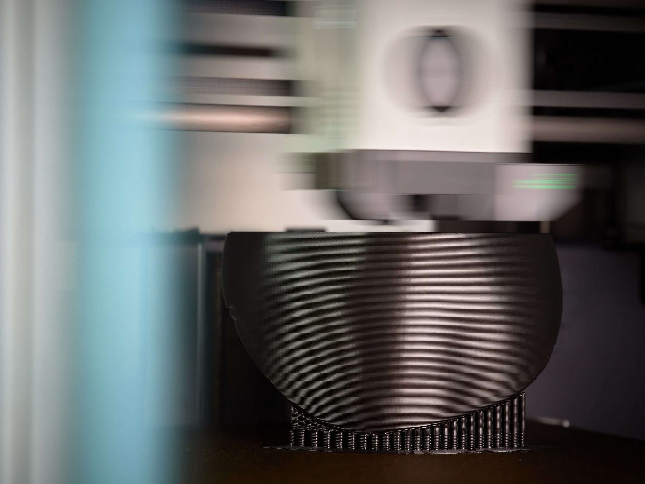 A scientific instrument with a black, textured surface in the foreground and a larger, white device with a circular opening in the background.