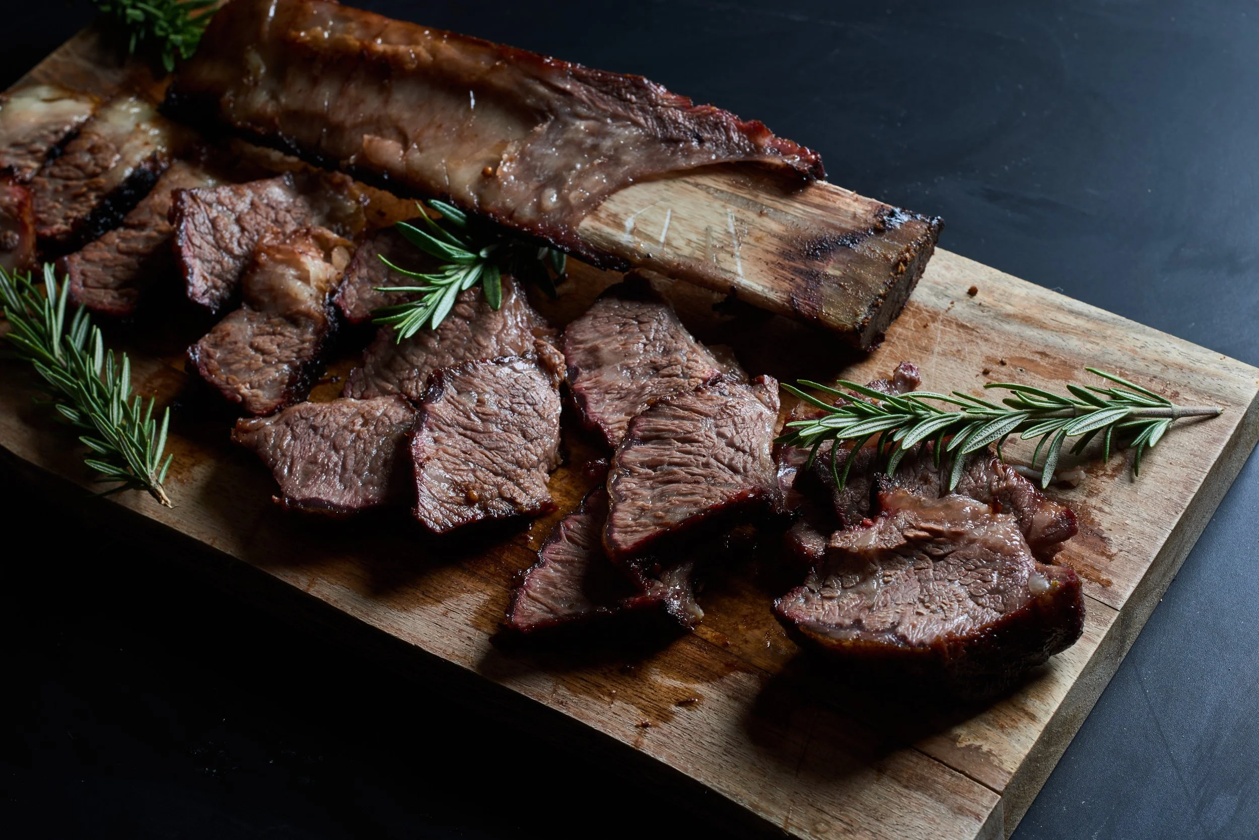 Slices of cooked beef brisket with herbs on a wooden cutting board.
