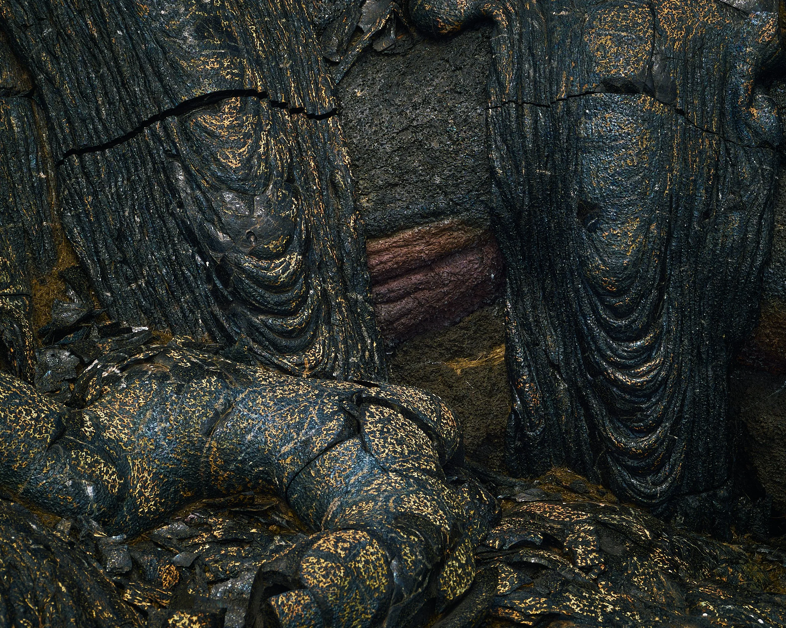 Close-up of dark volcanic rocks with streaks of orange and red, showing a rough and layered texture.