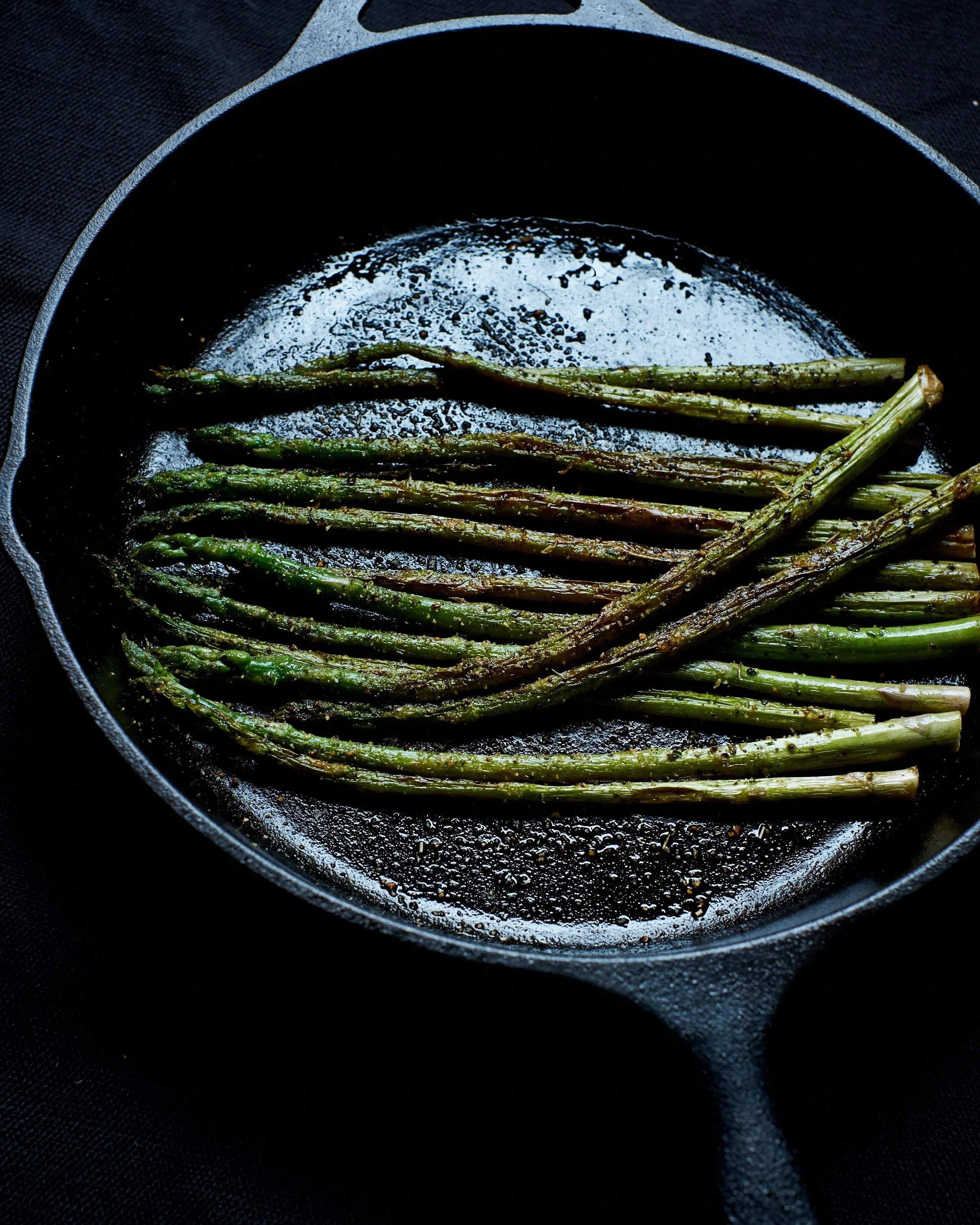Asparagus being cooked in a black cast iron skillet.