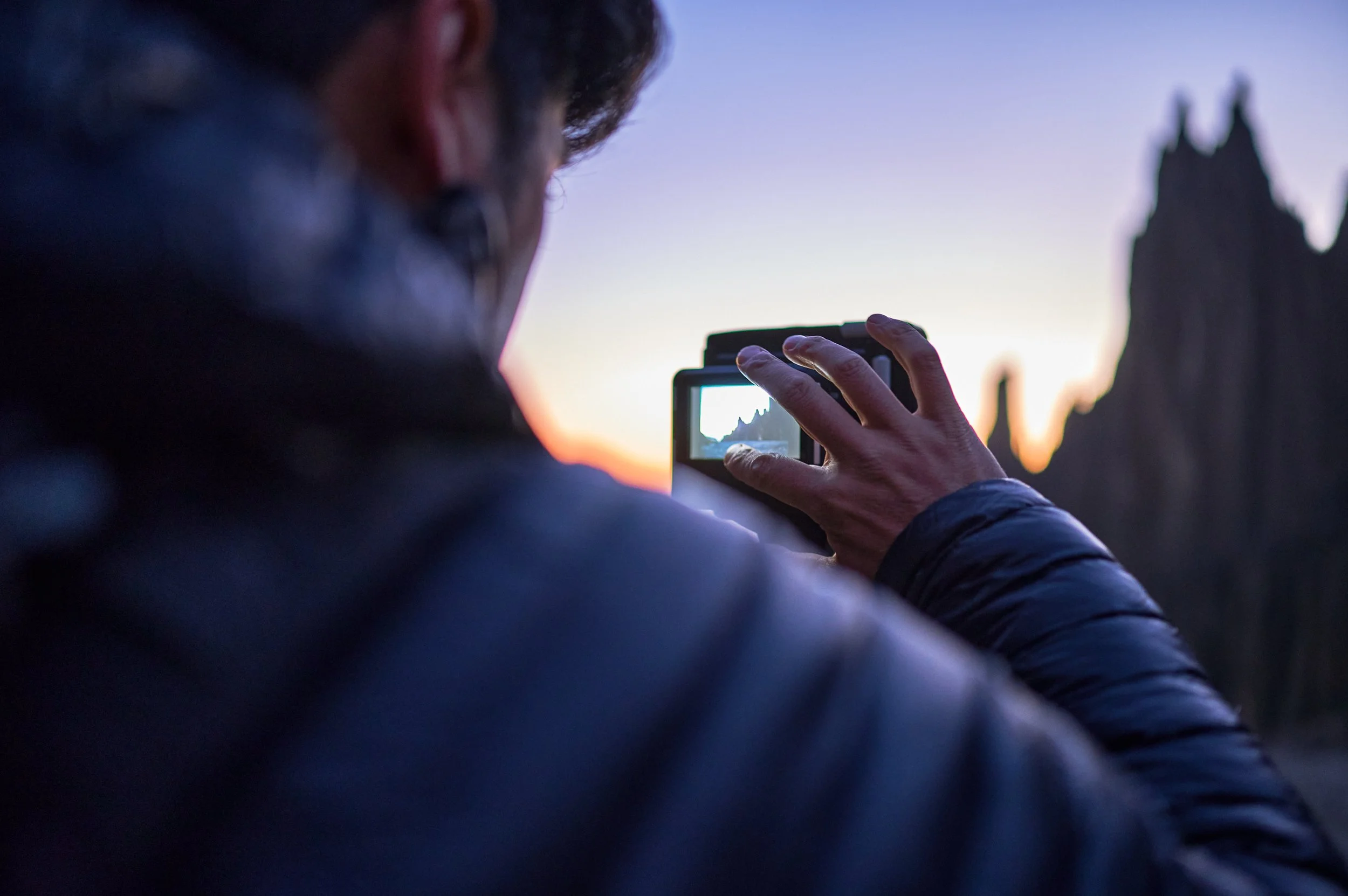 Person taking a photo of a mountain landscape during sunset or sunrise.