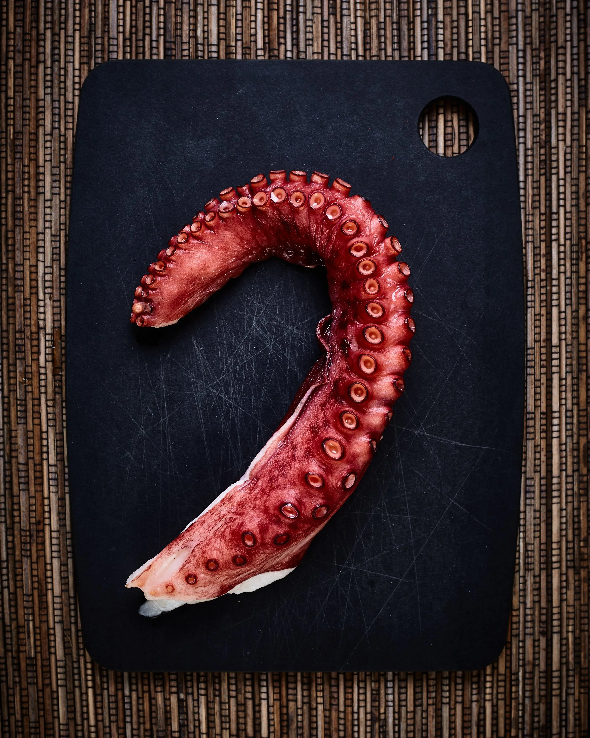 A raw octopus tentacle on a black cutting board.