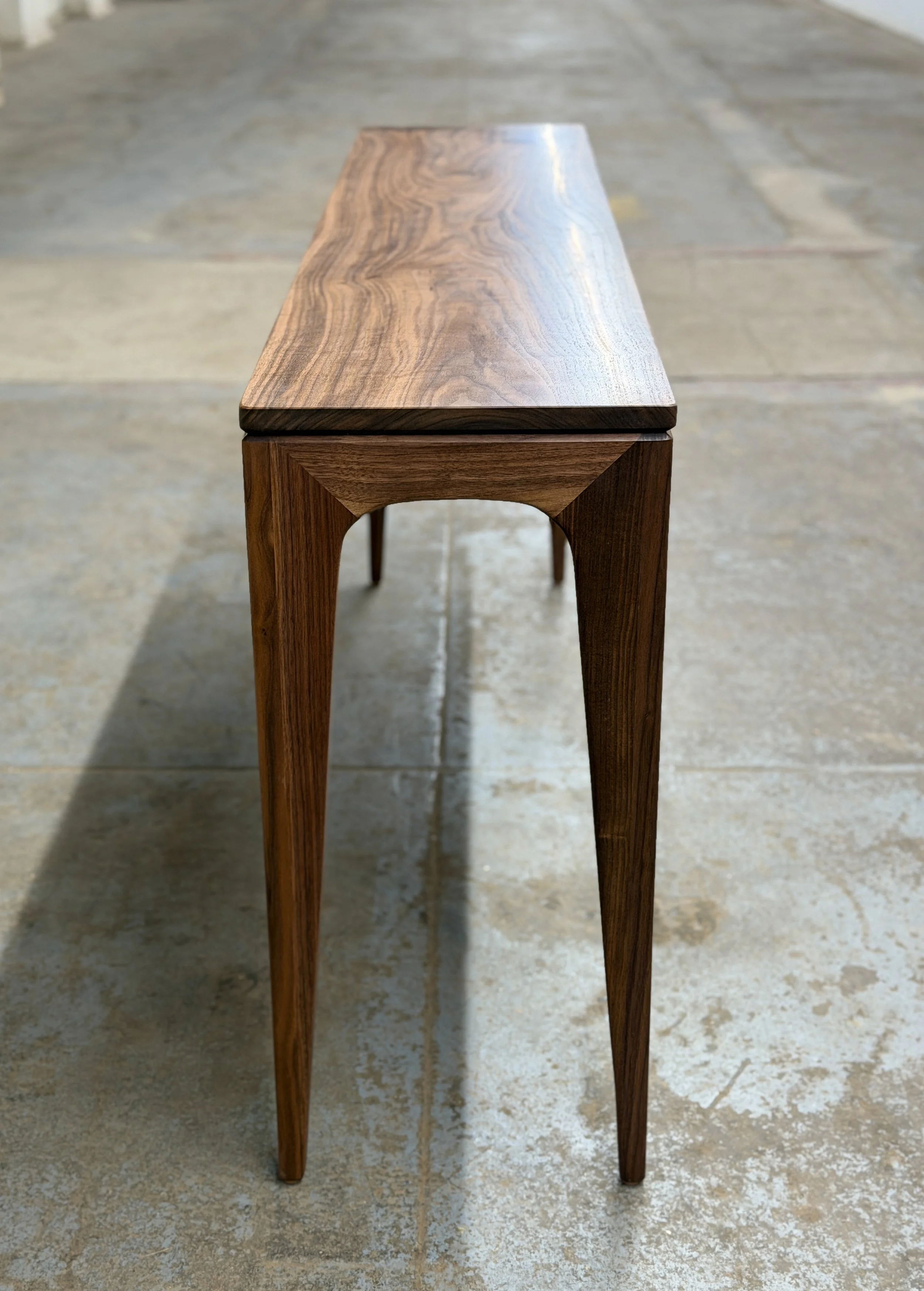 A wooden table with a sleek, minimalist design on a tiled floor.