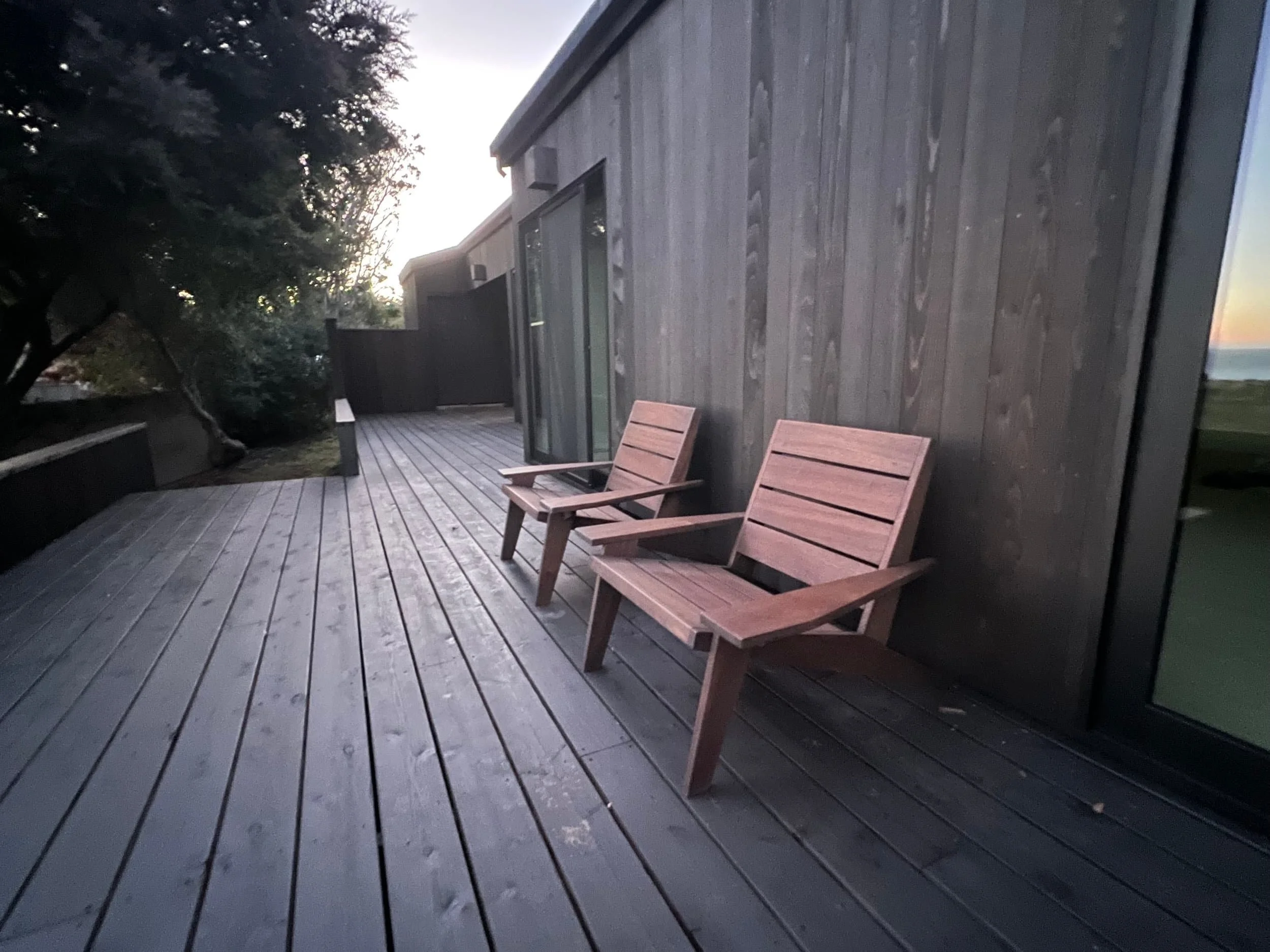 two wooden chairs on a wooden deck outside a modern house at dusk