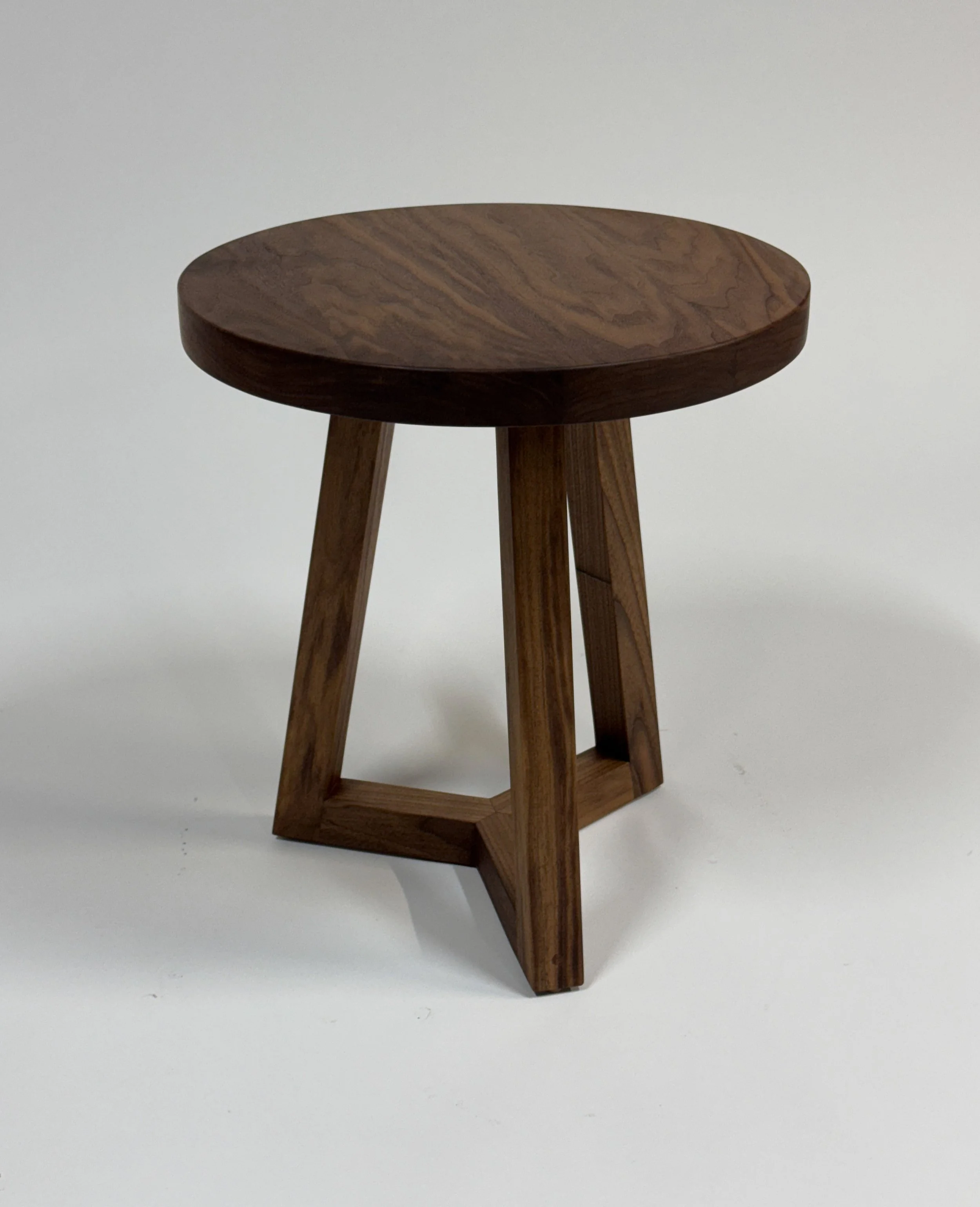 A small wooden stool with a round top and three angled legs on a white background.