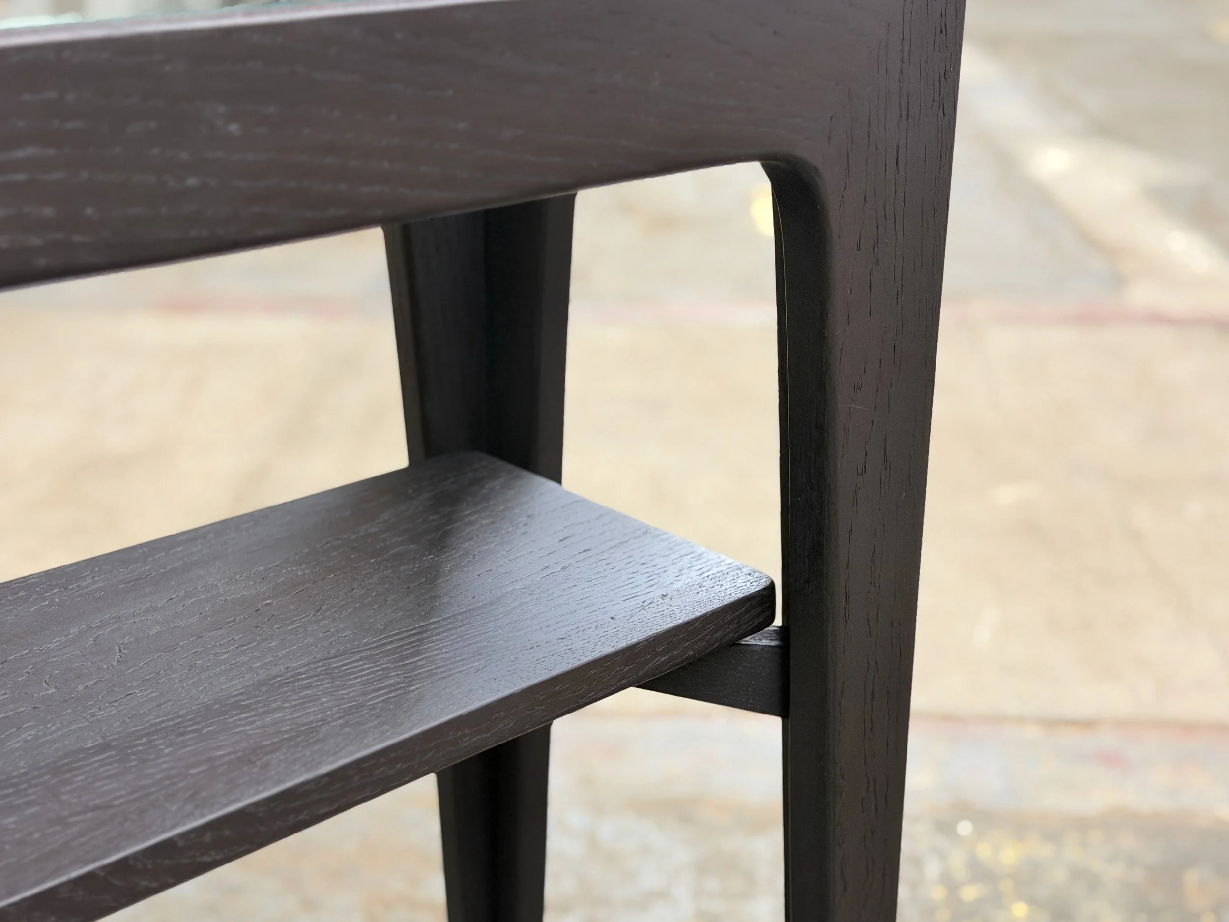 Close-up of dark brown wooden table with a shelf and vertical support, on a concrete surface.