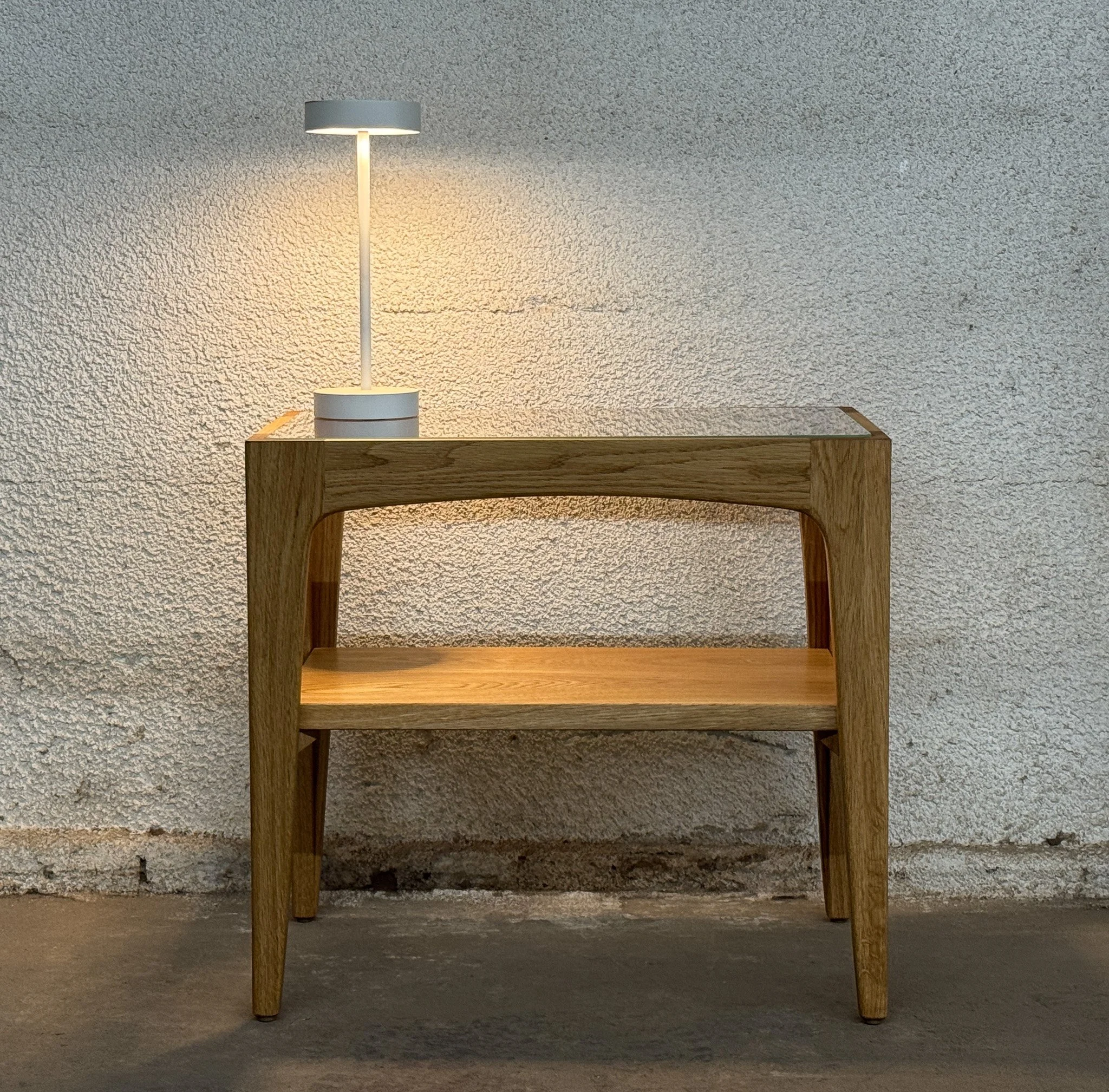 A wooden side table with a lamp on top and a textured wall background.