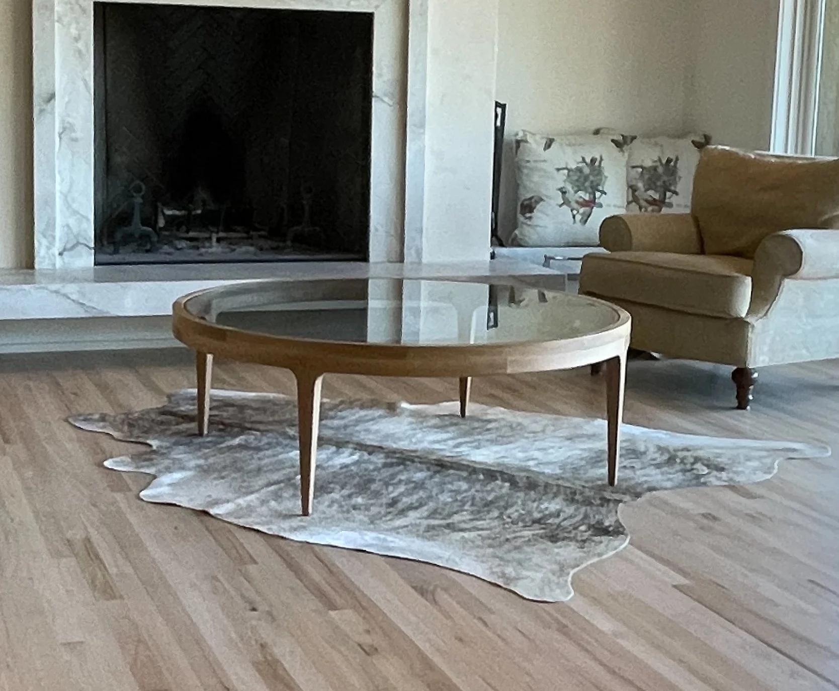 Living room with a fireplace, a beige armchair, a cowhide rug, and a round coffee table.