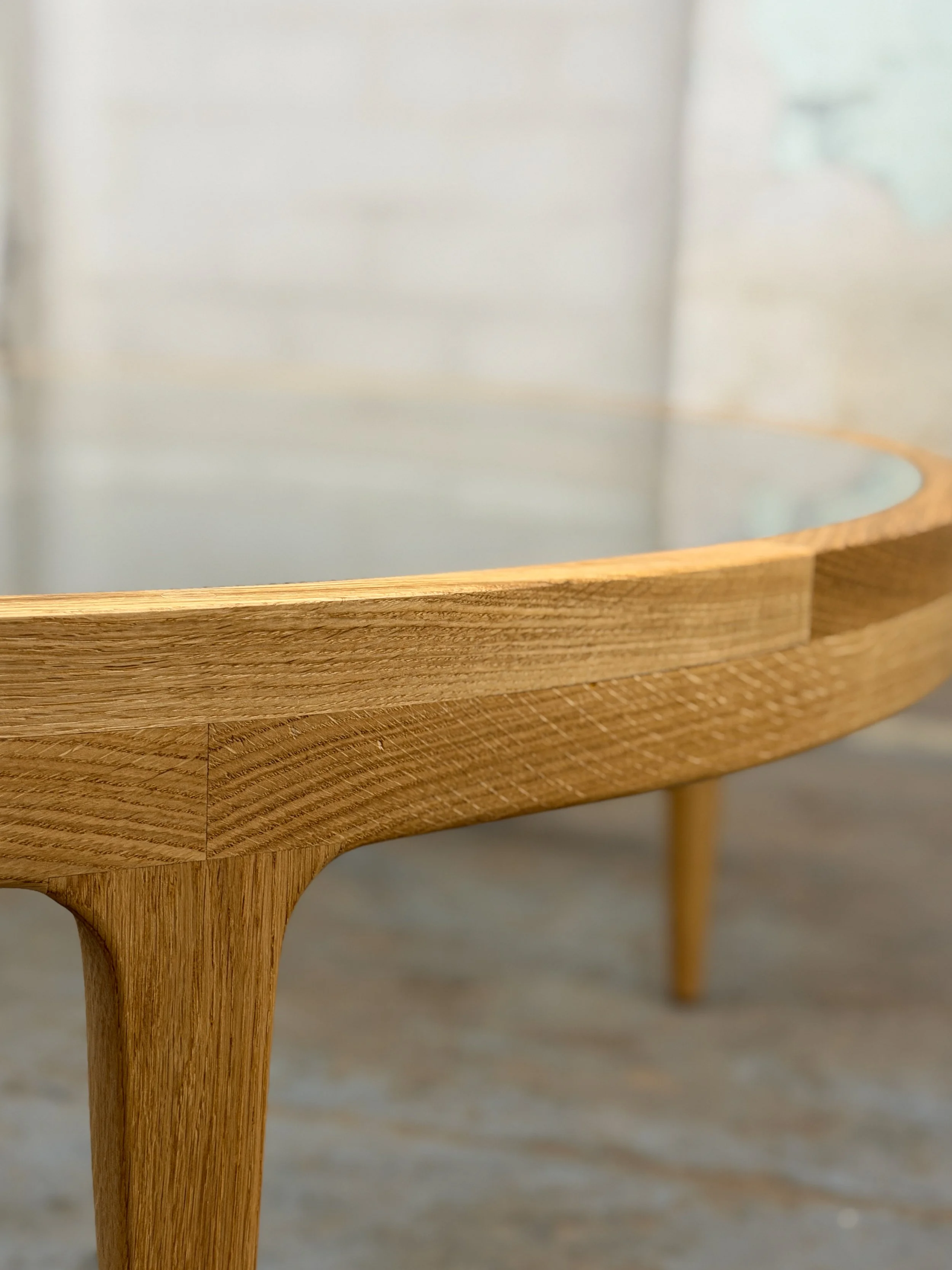 Close-up of a wooden table with a glass top, showing the wood grain and one leg in the foreground.
