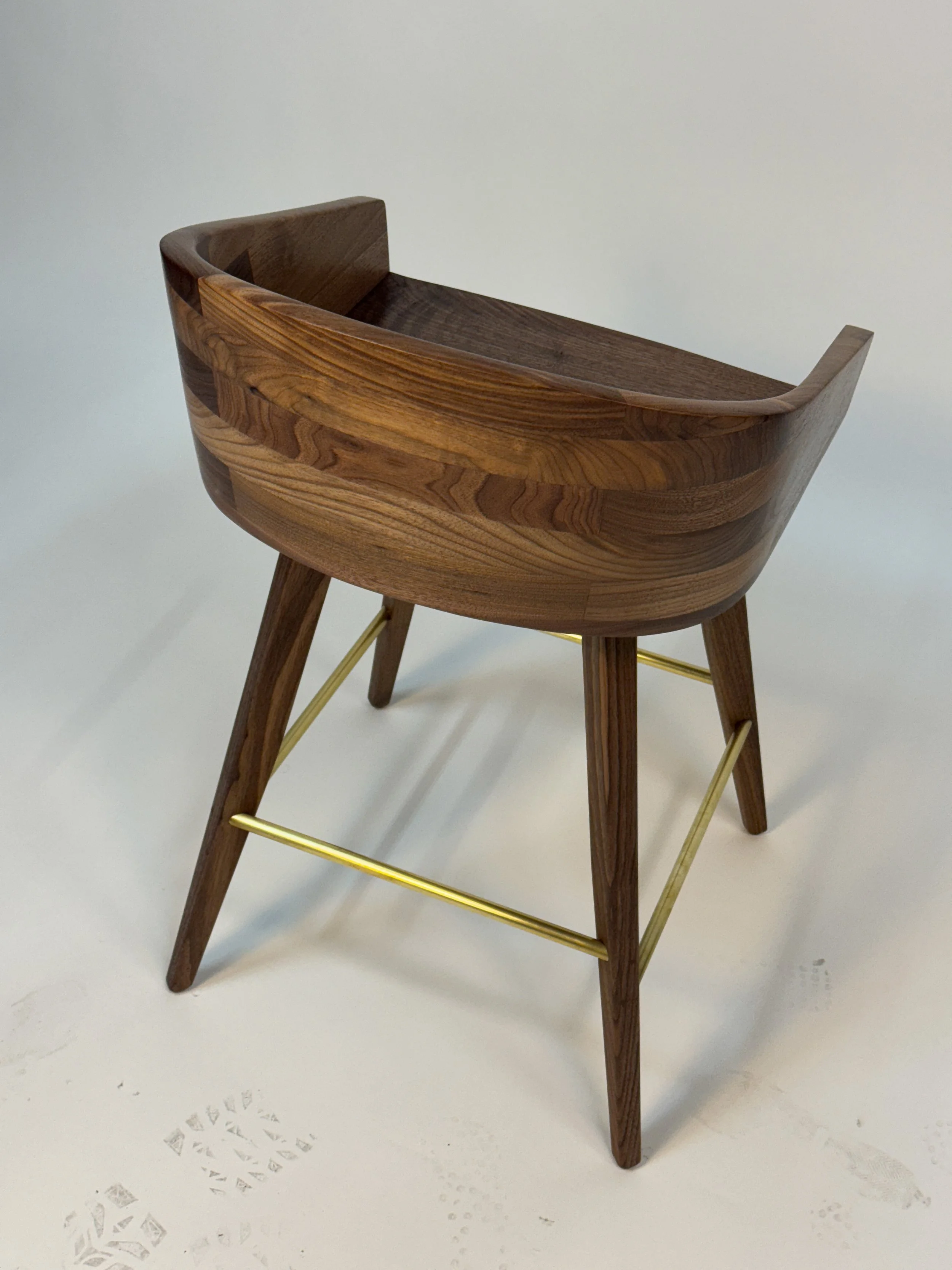 A wooden chair with a curved seat and backrest, supported by four angled legs connected by gold-colored metal bars.