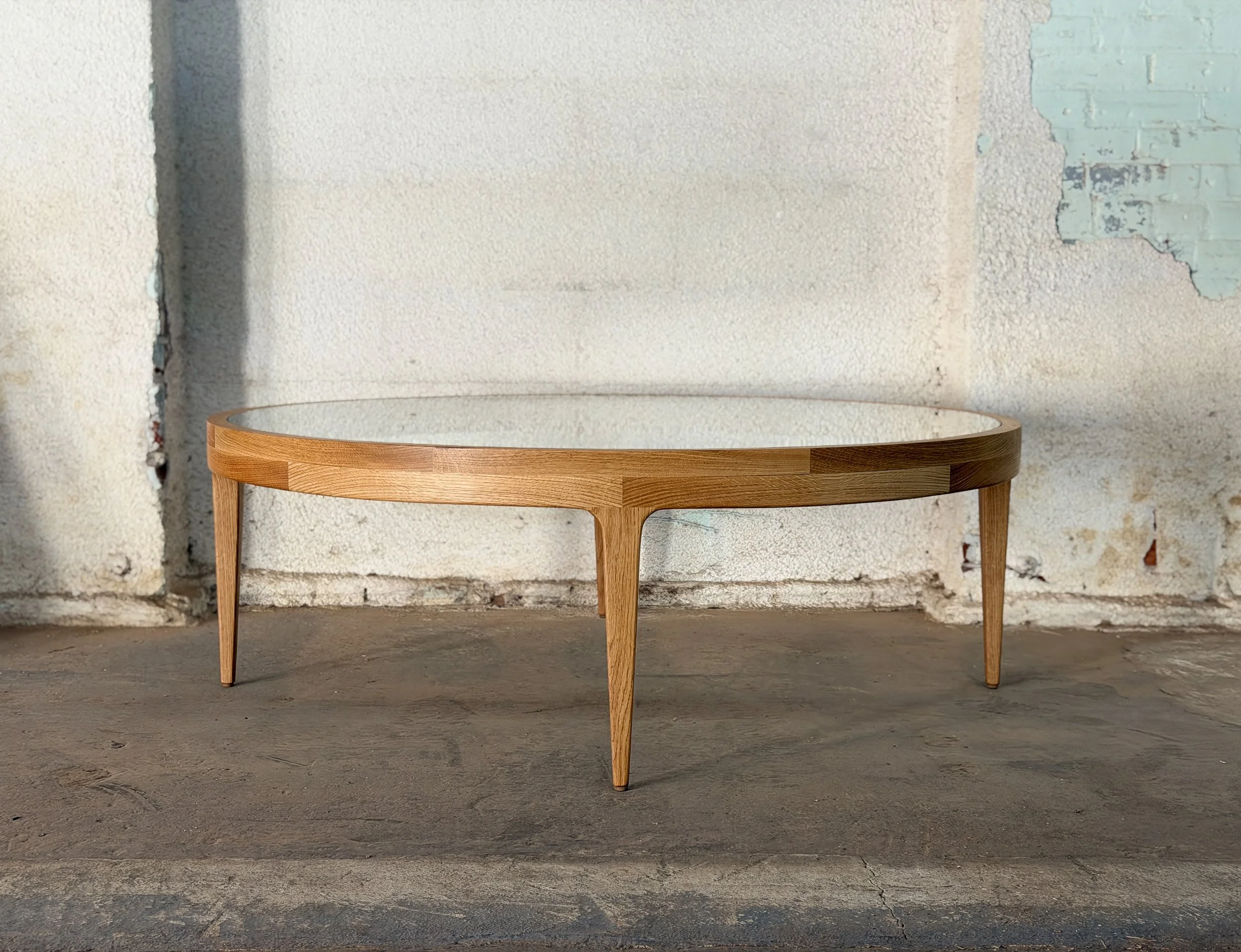 A wooden coffee table with a glass top against a textured, partially peeling wall.