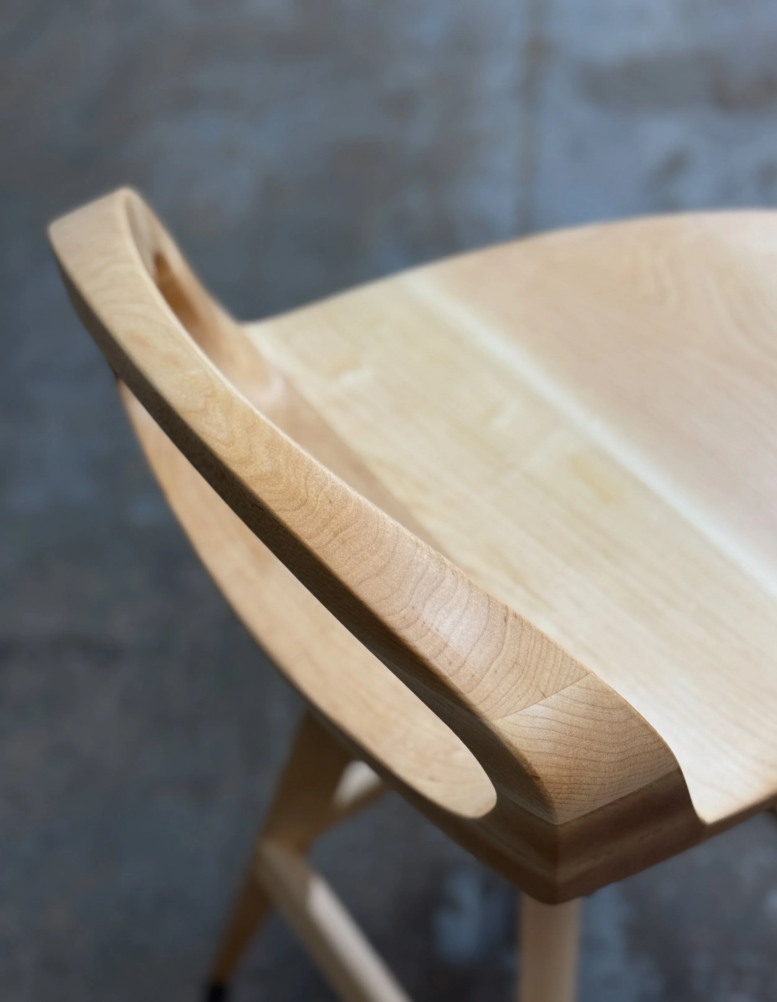 Close-up of a wooden chair with curved backrest, showing wood grain detail, against a blurred dark background.
