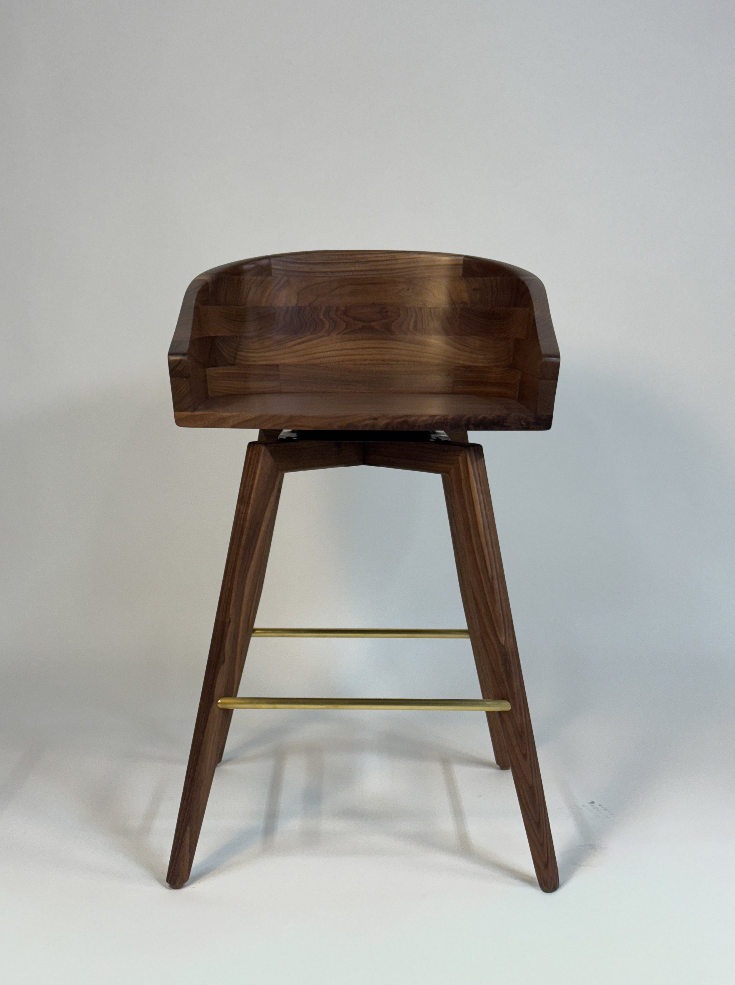 A wooden barstool with a curved seat and four legs connected by gold-colored horizontal bars, placed against a plain light-colored background.