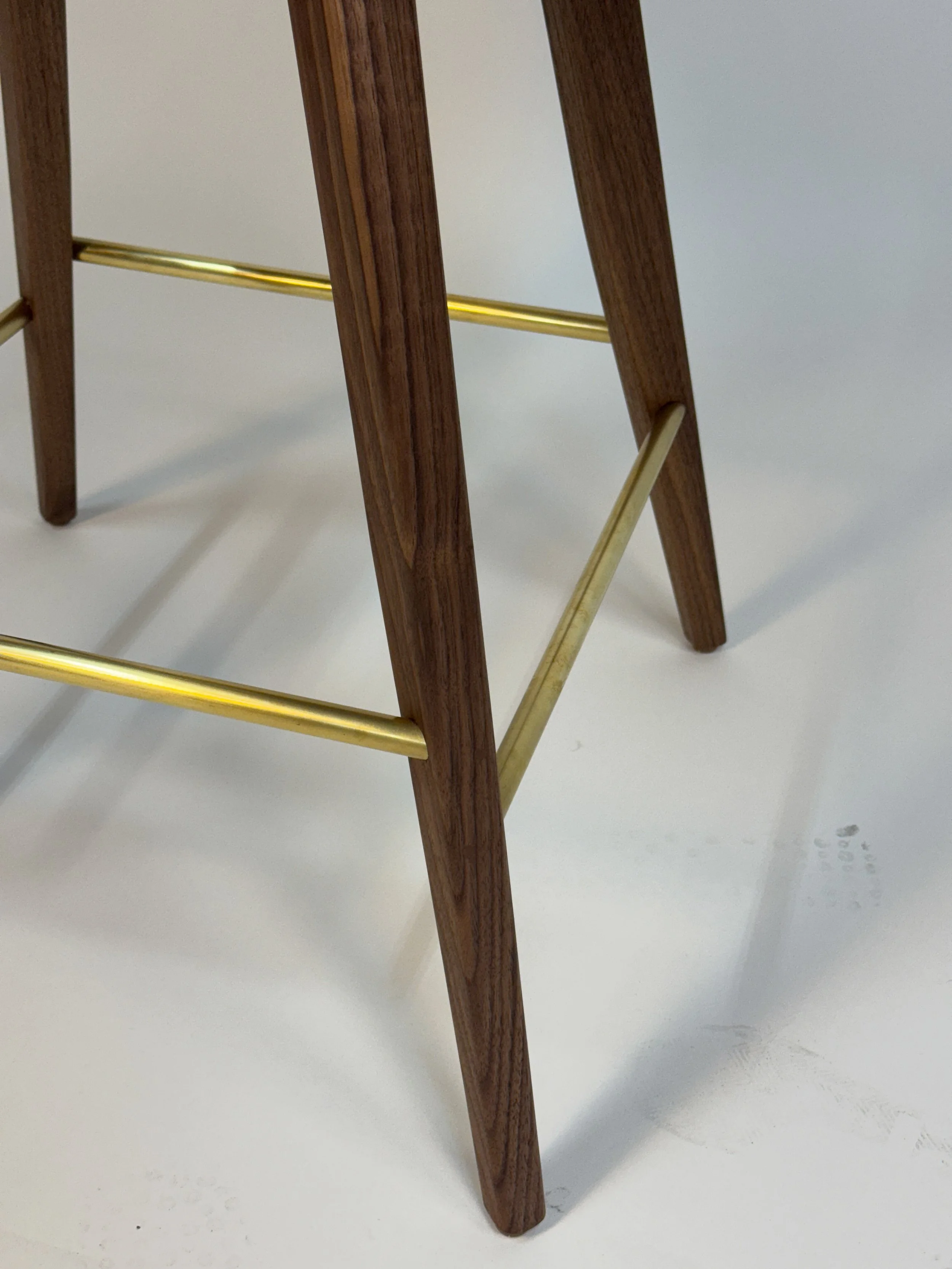 Close-up of wooden chair legs with gold-colored metal support bars on a white surface.